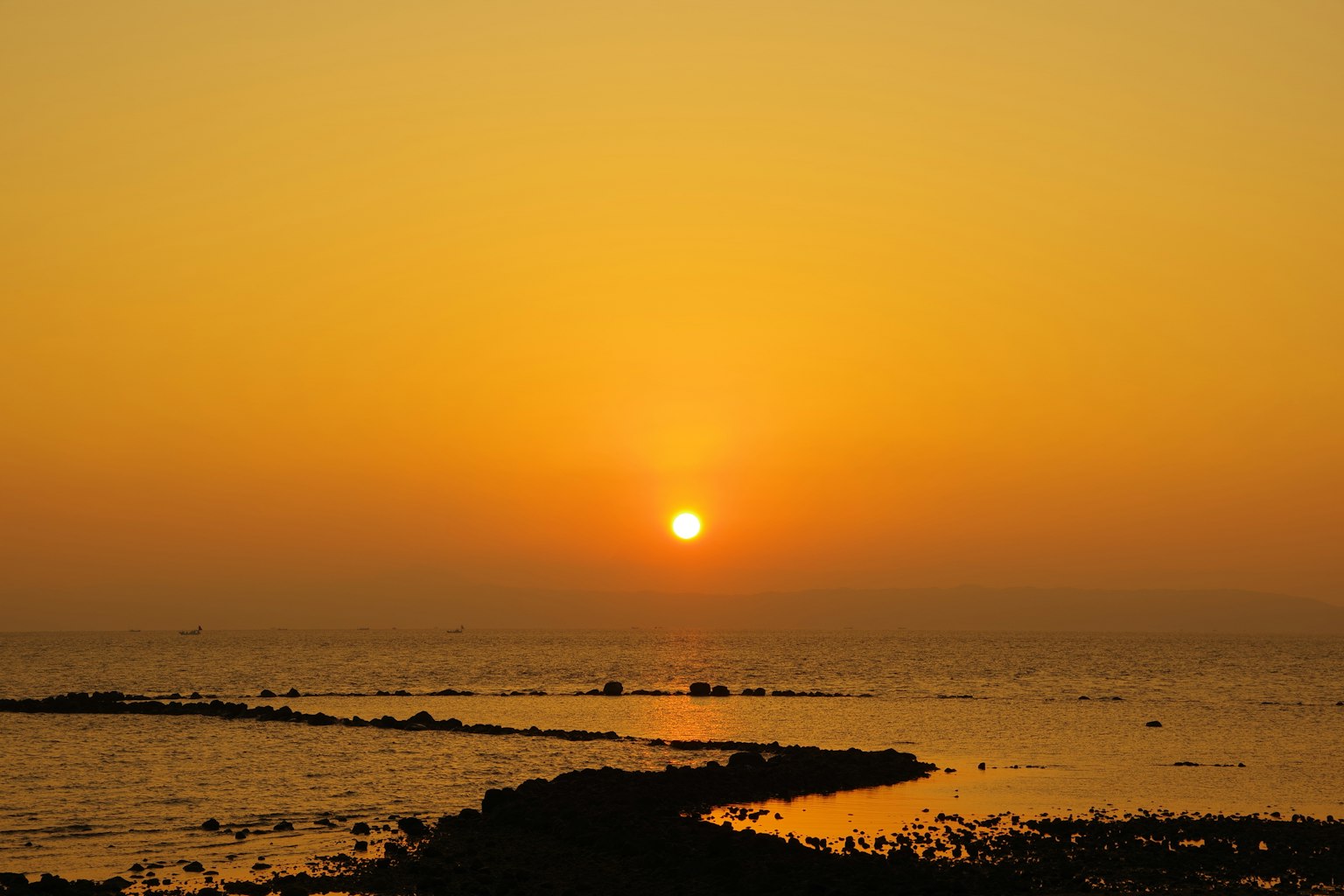 Coucher de soleil sur la mer calme avec un ciel orange et la silhouette de rochers