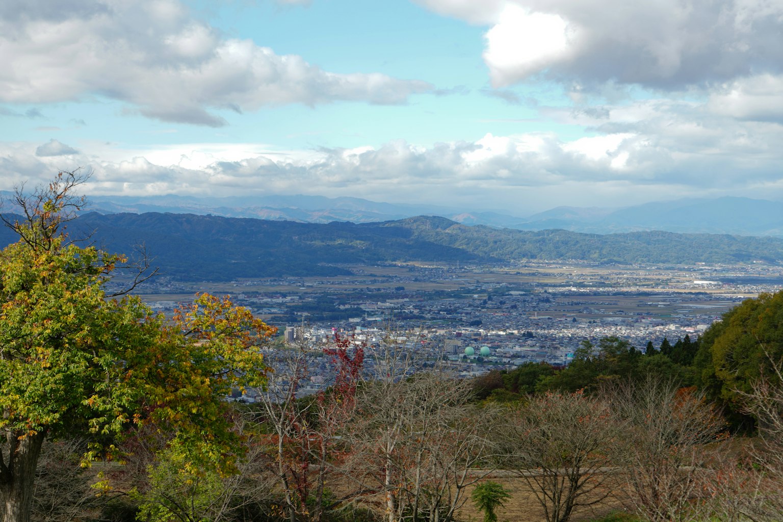 Vista panoramica di montagne e valli sotto un cielo nuvoloso con alberi colorati