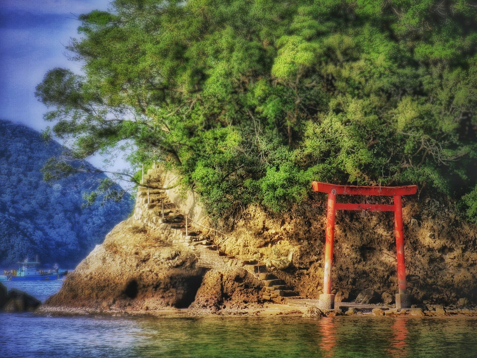 Portail torii rouge se tenant sur une côte rocheuse avec une végétation luxuriante et une mer calme