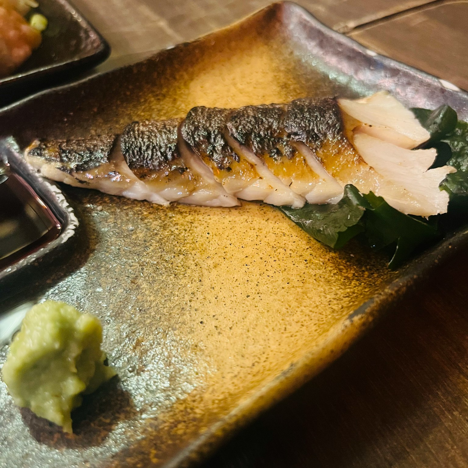 Filet de poisson grillé servi sur une assiette décorative avec du wasabi
