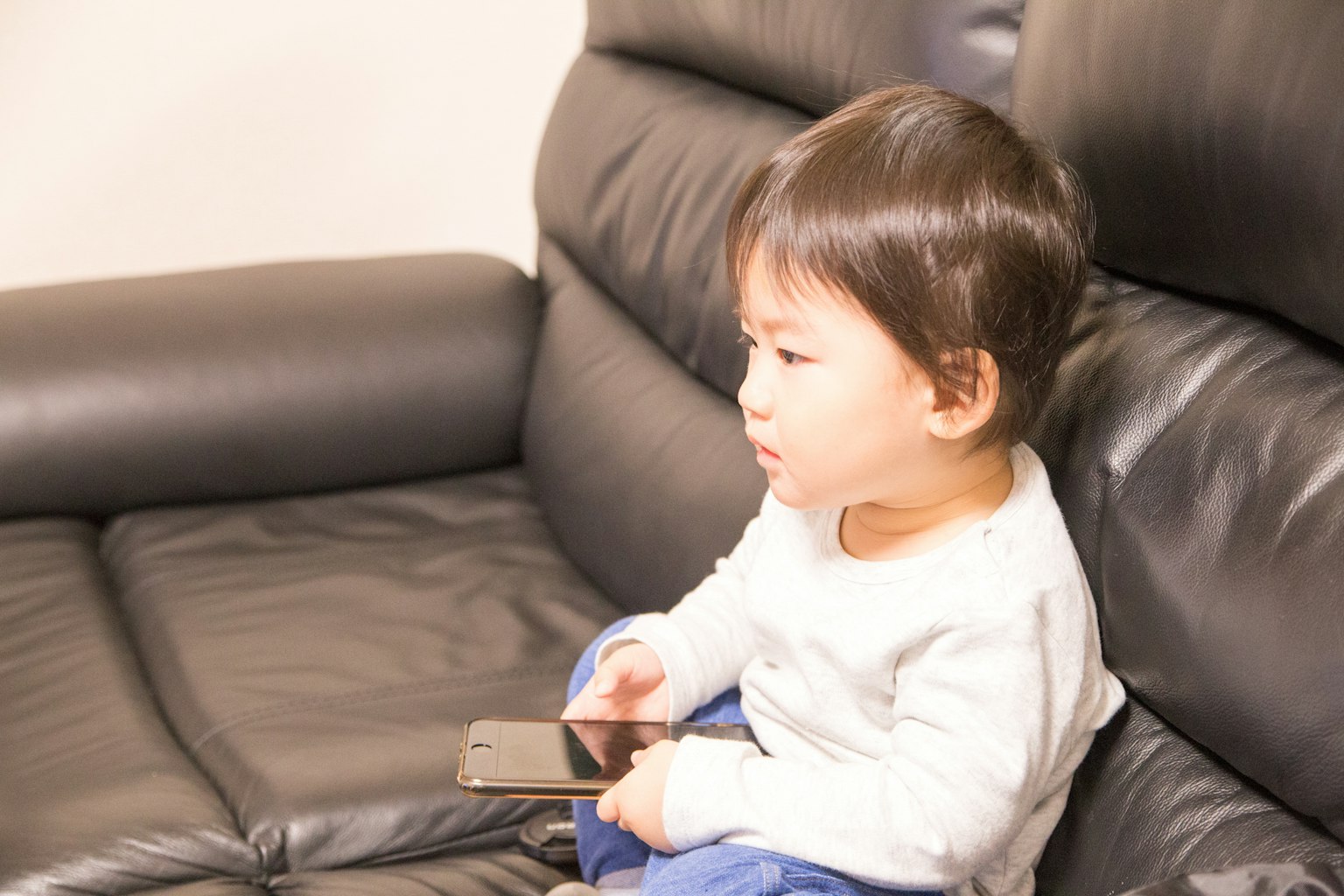 Niño sentado en un sofá negro sosteniendo un teléfono inteligente