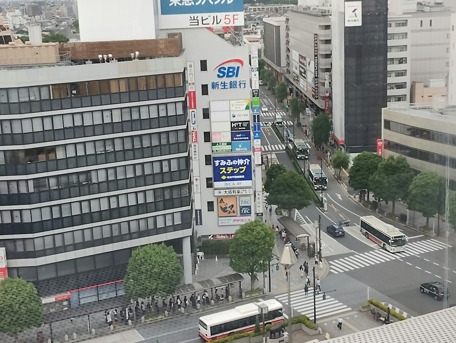城市景觀，高樓和繁忙街道，人們在斑馬線上等候，顯眼的SBI標誌