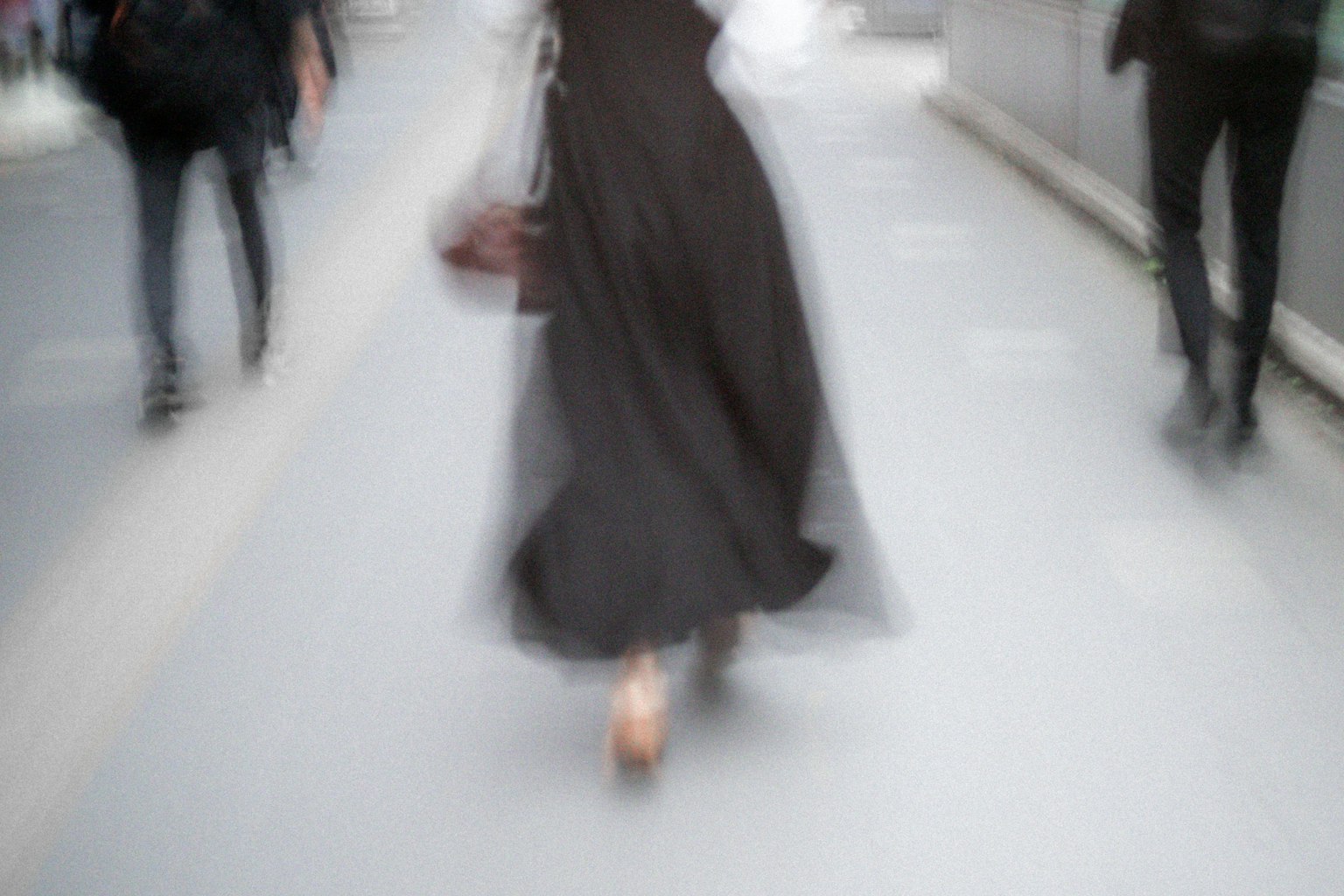 Una donna in abito nero che cammina in un ambiente urbano sfocato