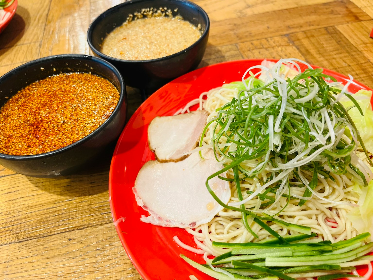 Cold noodles served on a red plate with green onions and slices of pork