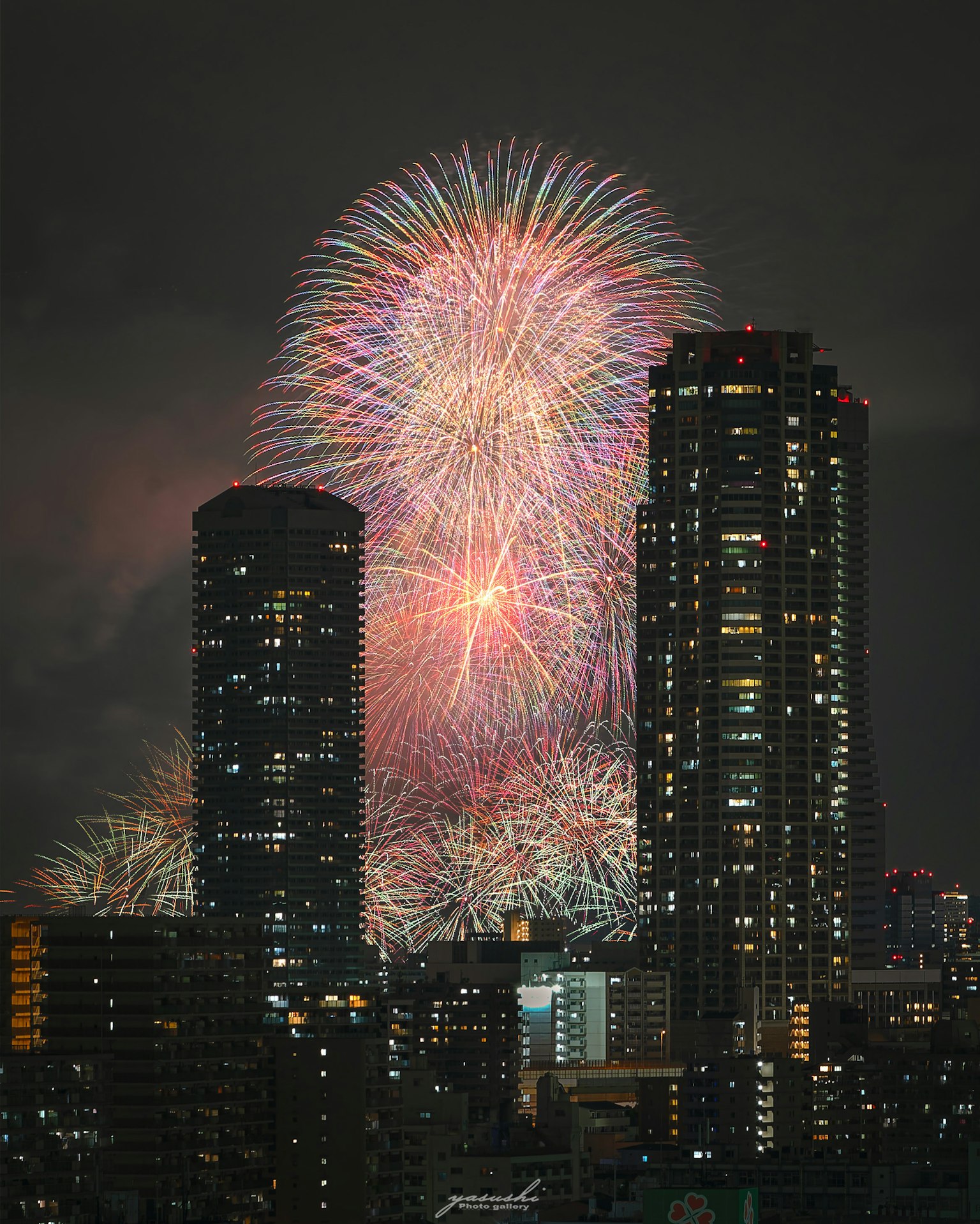 夜空に花火が打ち上げられ高層ビルの間から見える