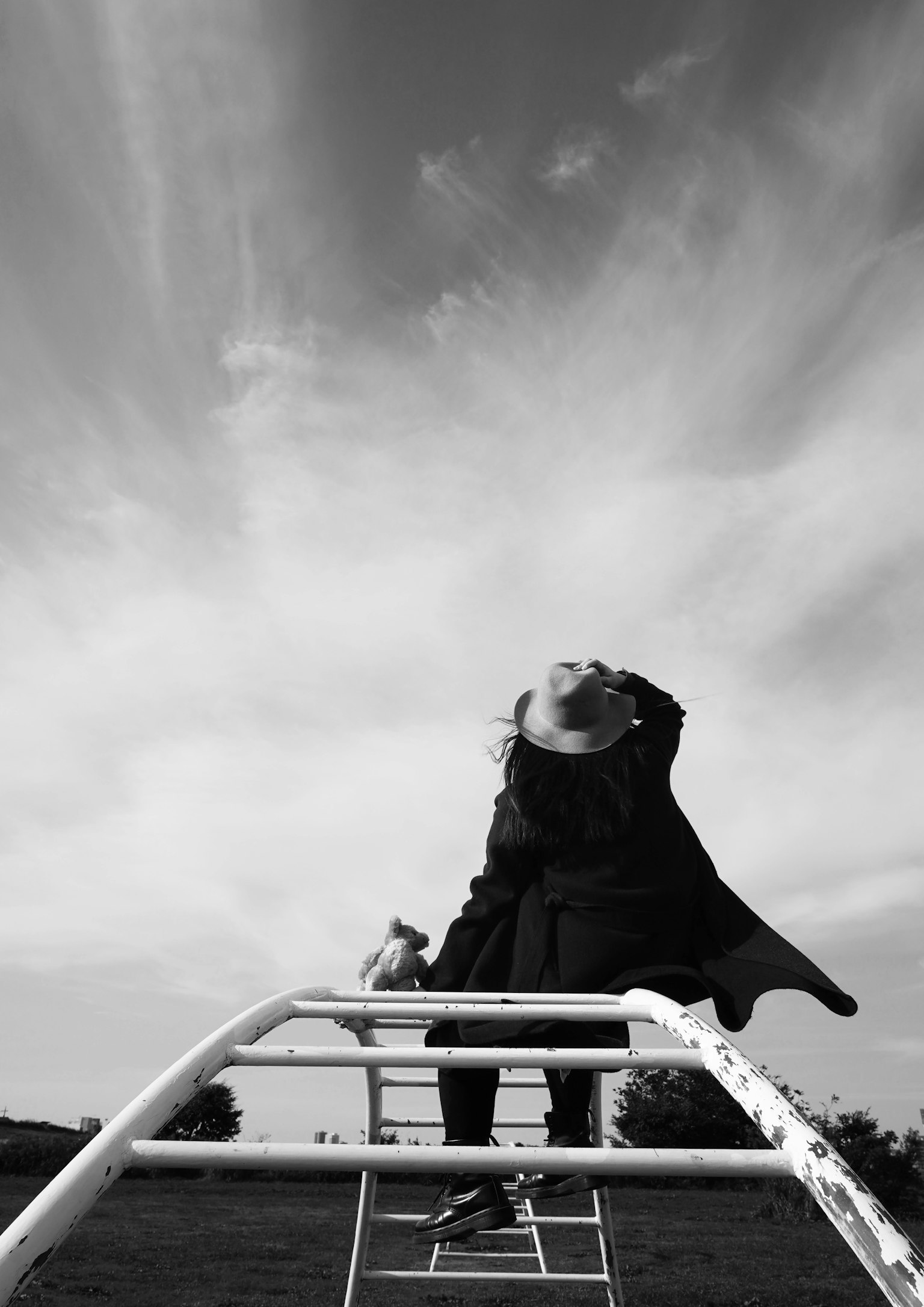 Anak berpakaian hitam berdiri di atas peralatan bermain di bawah langit biru