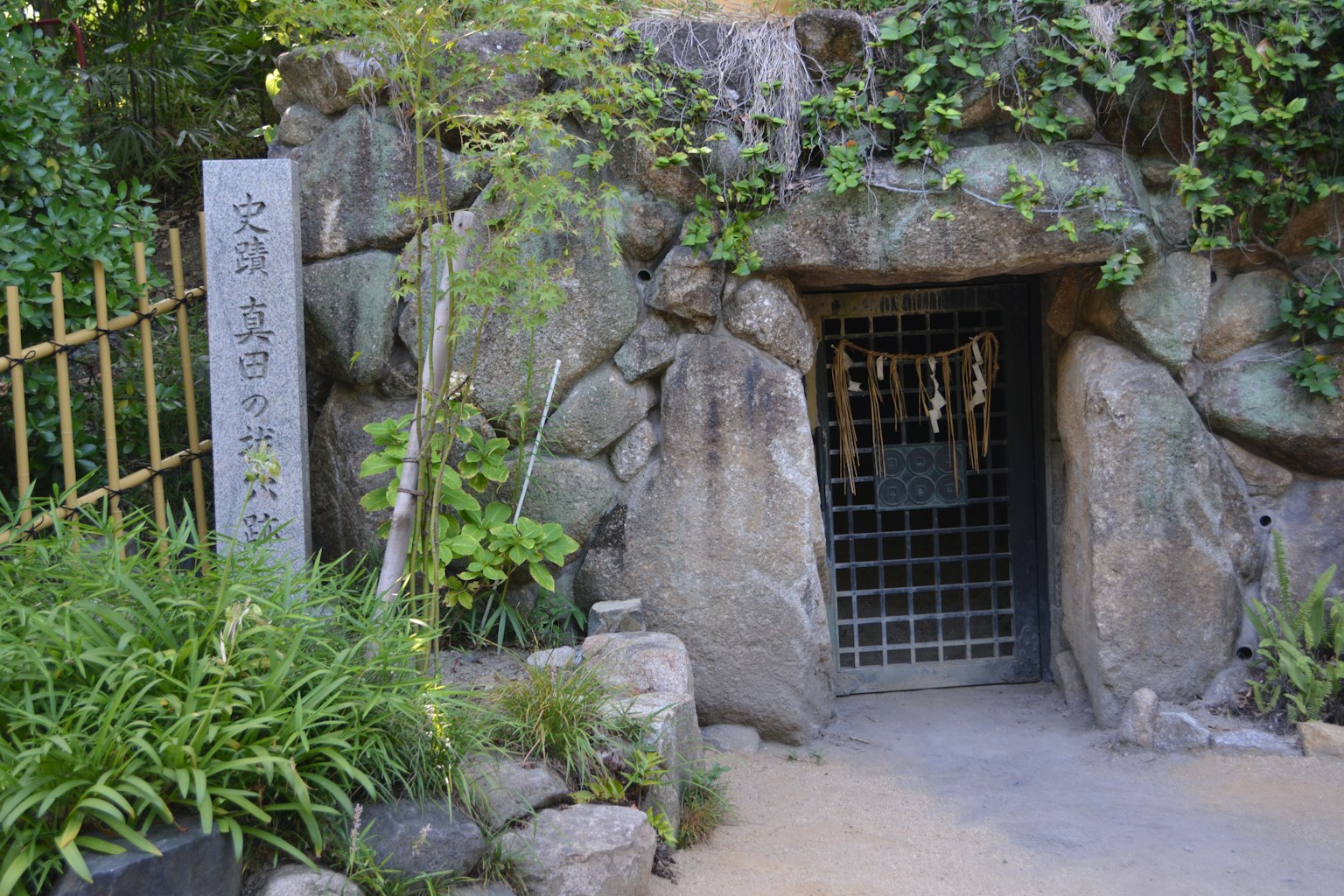 Stone entrance surrounded by greenery with a metal gate