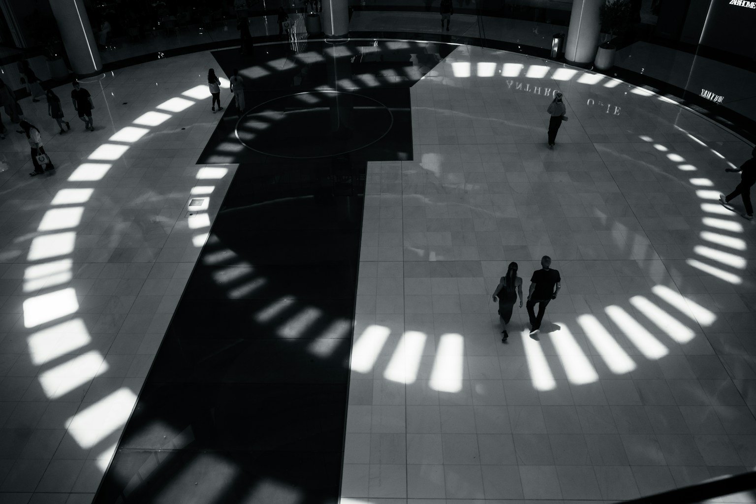 Orang-orang berjalan di atas lantai melingkar dengan kontras cahaya dan bayangan