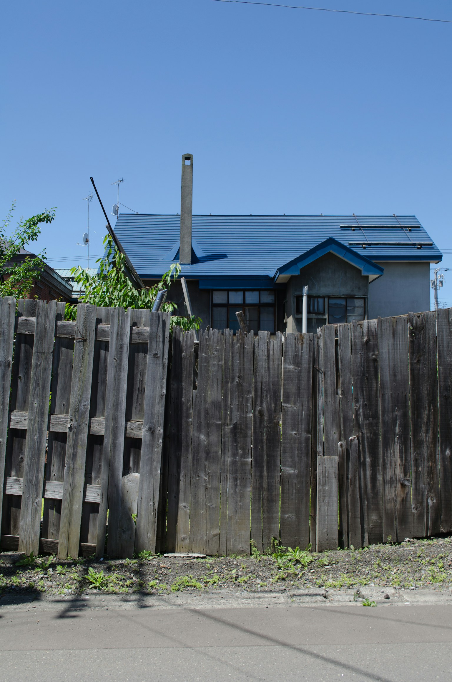 Una casa con un tetto blu e una vecchia recinzione in legno in primo piano