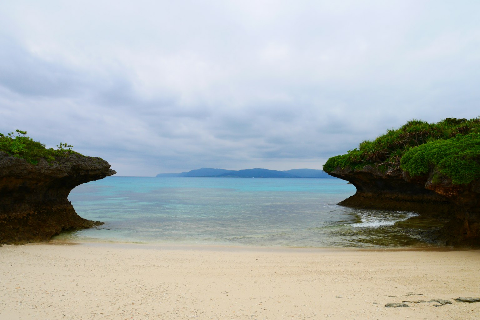 ทิวทัศน์ชายหาดสงบที่ถูกล้อมรอบด้วยทะเลสีน้ำเงินและทรายขาว