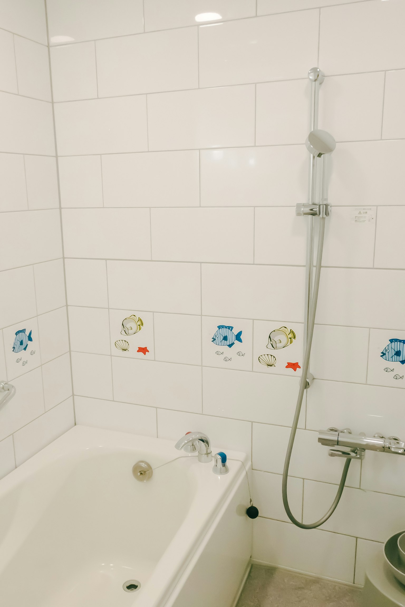 Badezimmer mit weißen Fliesen mit Badewanne und Dusche Kinderfischillustrationen auf den Fliesen