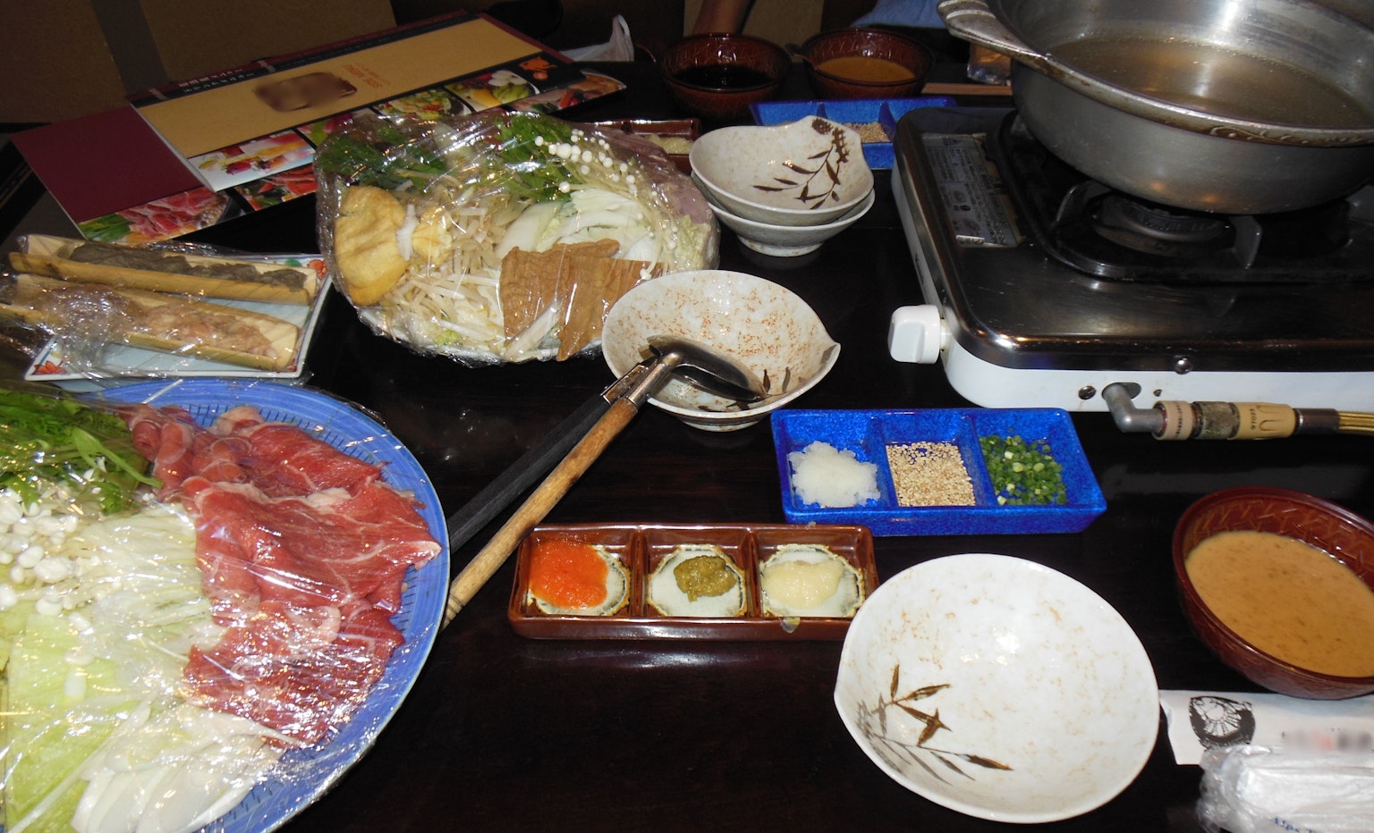 Meja yang disiapkan dengan bahan-bahan untuk hot pot dan saus