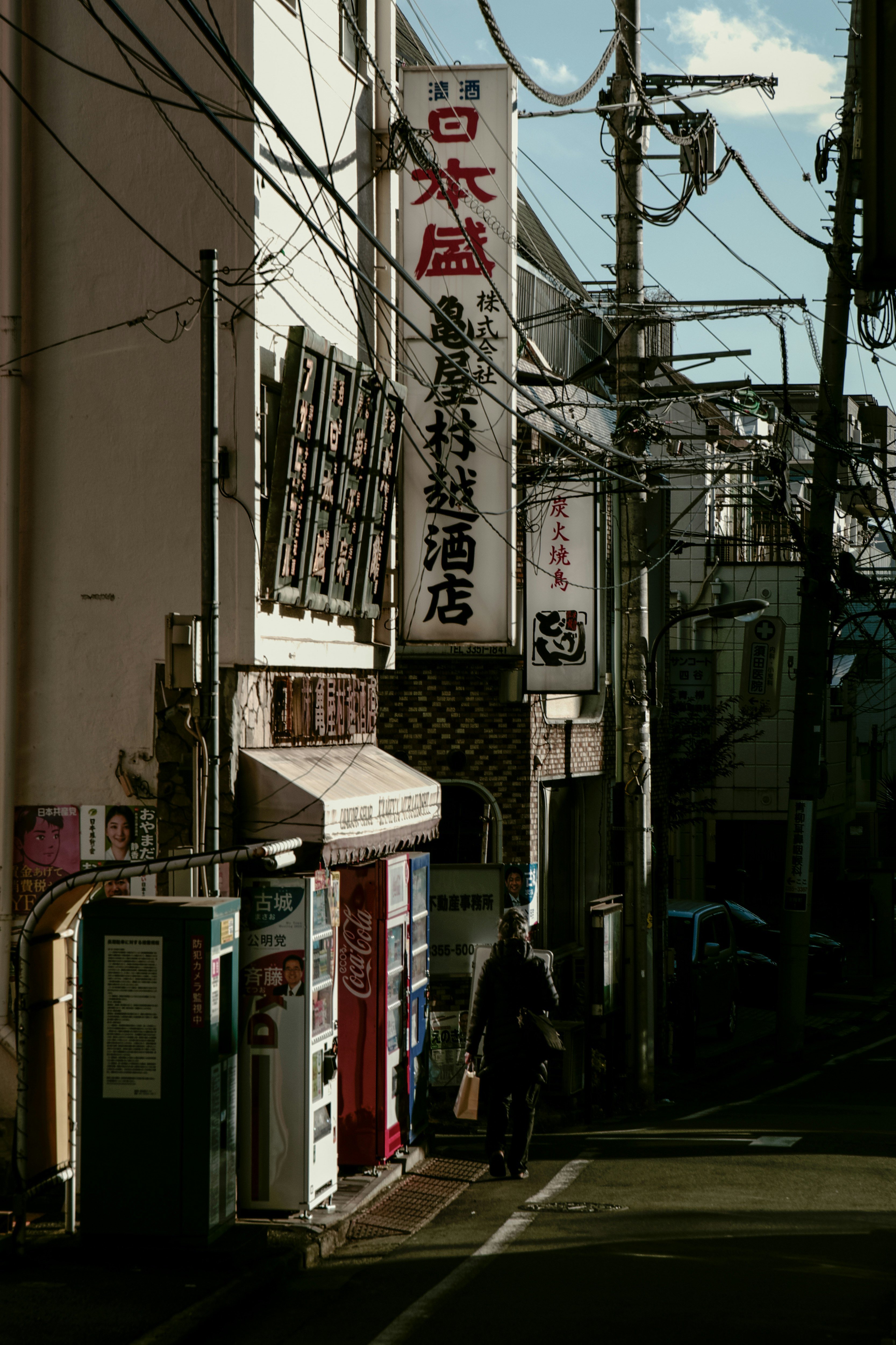 路地に並ぶ看板と自動販売機のある商店街の軒先