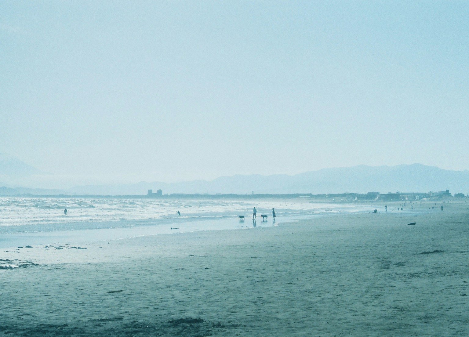 Scena costiera con persone che si godono la spiaggia e le onde sotto un cielo blu