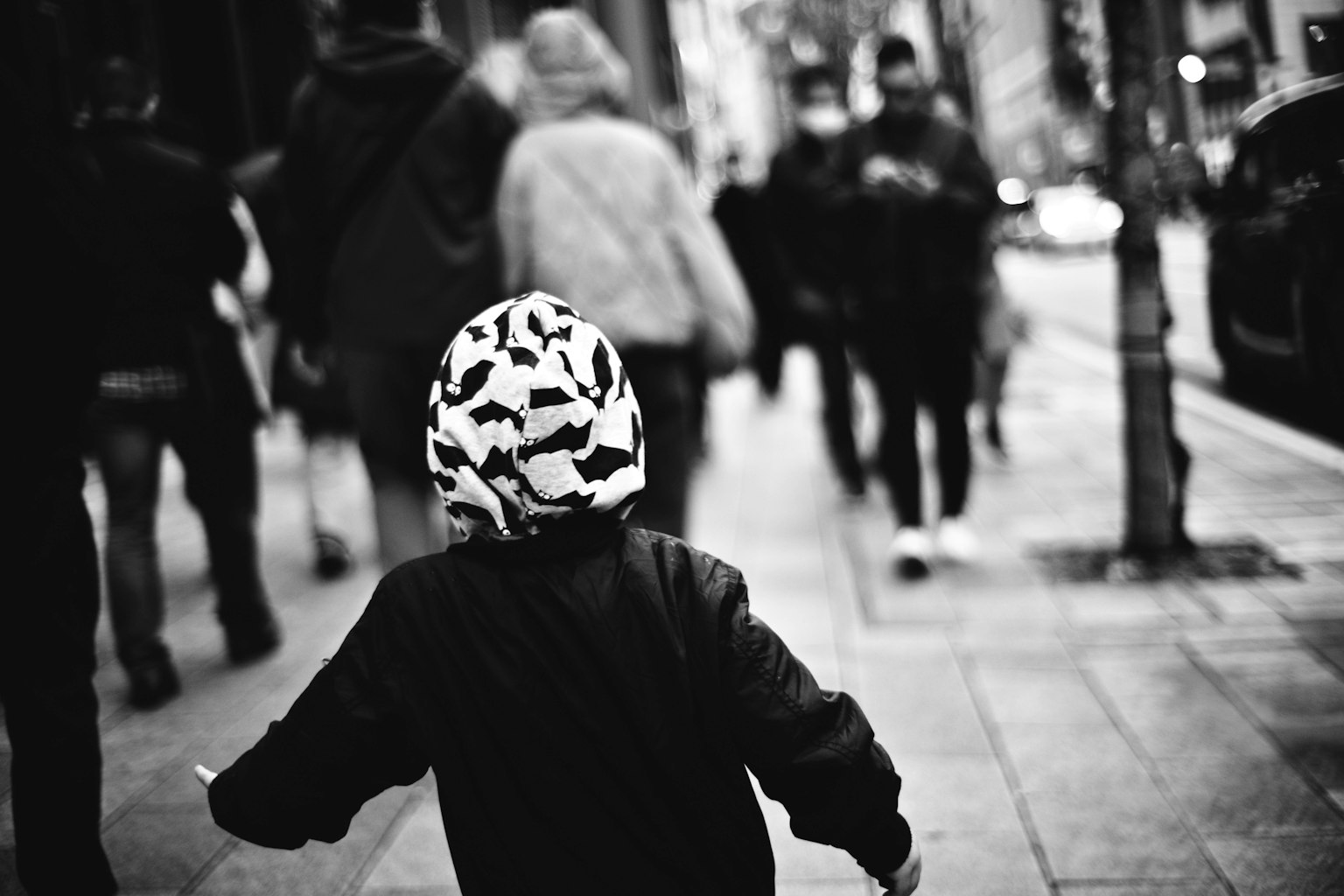 Bambino che corre in una strada in bianco e nero con persone che camminano intorno