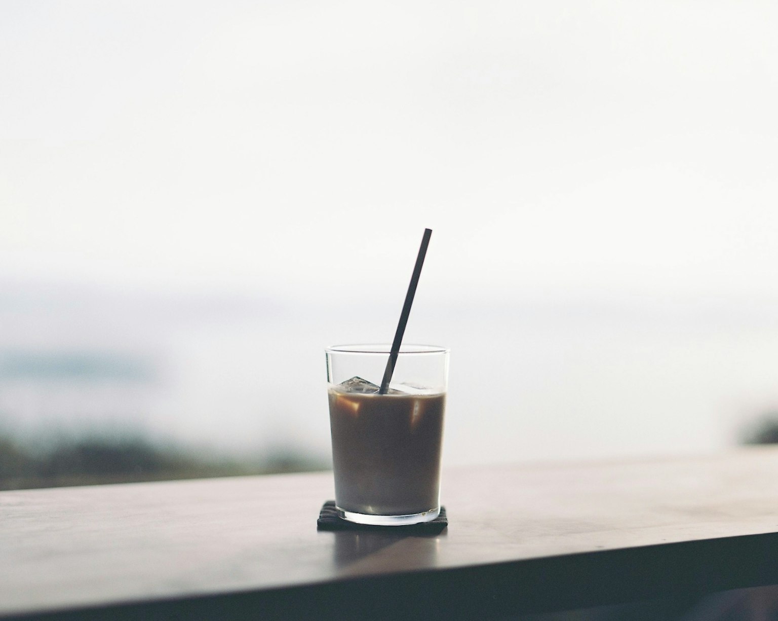 Un bicchiere di caffè freddo con una cannuccia su una superficie di legno vicino alla finestra