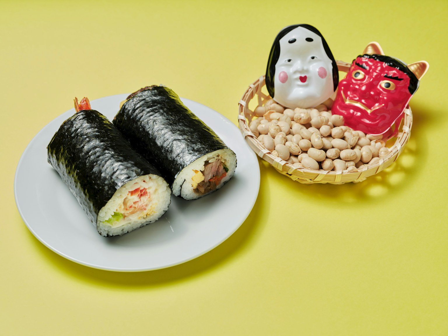Roti sushi di atas piring putih dengan figur karakter Jepang tradisional di latar belakang kuning