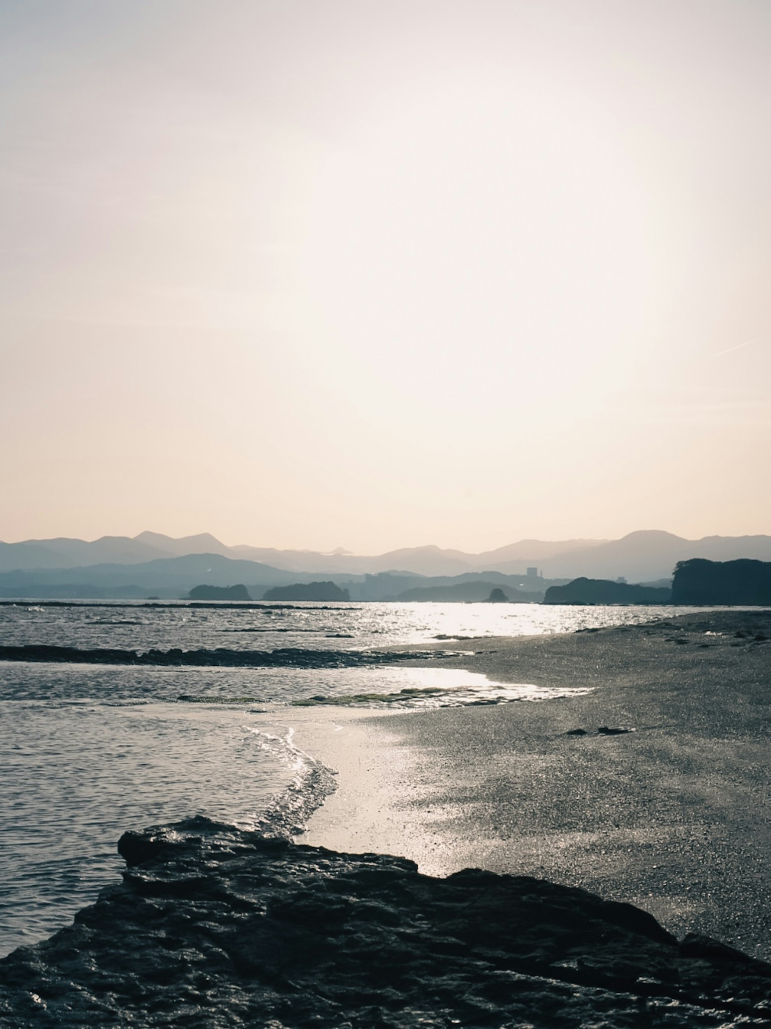 Sunset over the sea with mountains in the background rocky foreground and calm water
