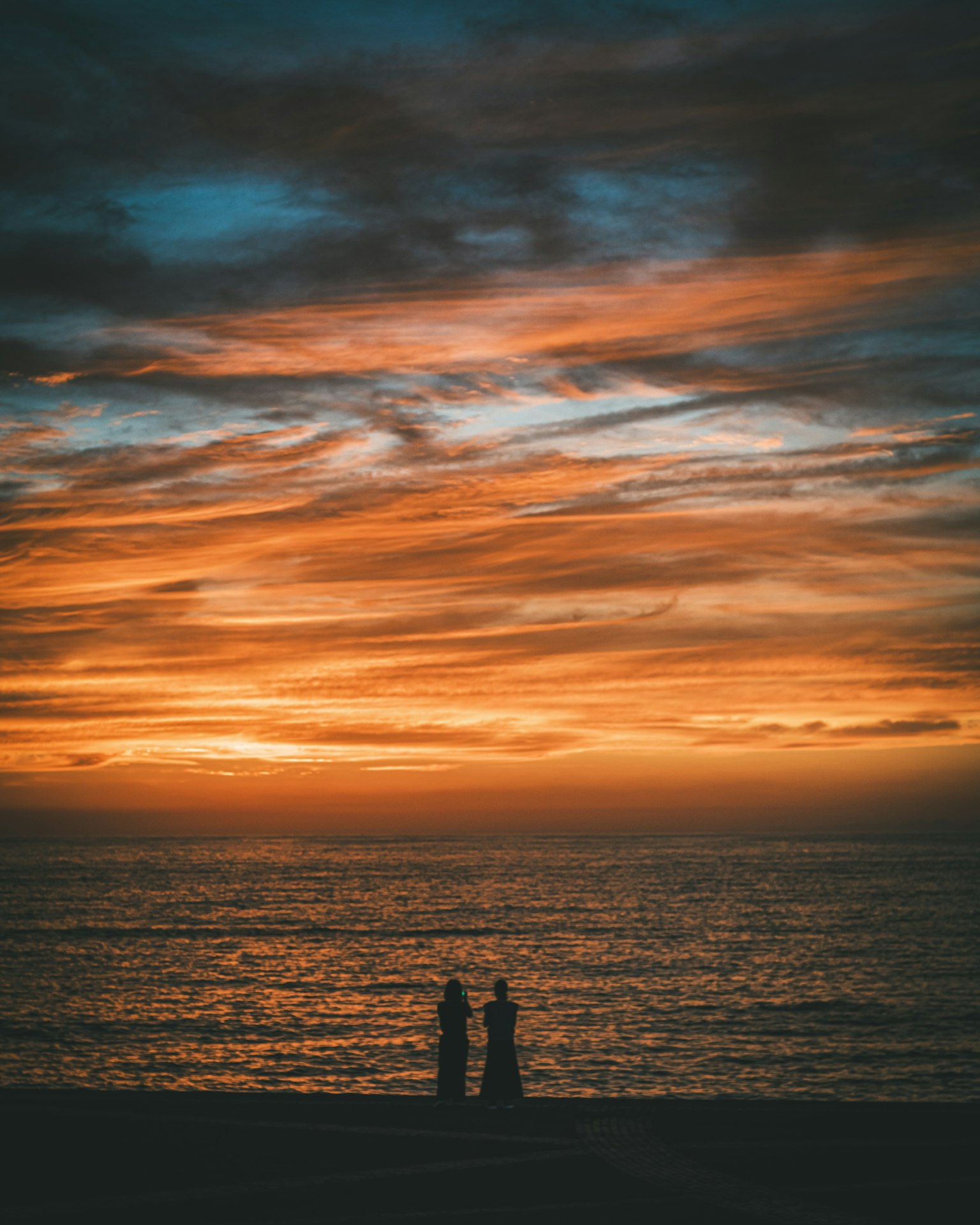 Silueta de dos personas de pie junto al mar al atardecer