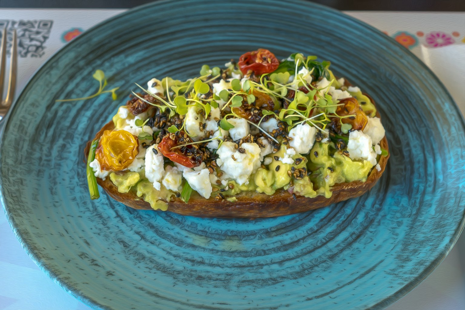 Toast di avocado su un piatto blu guarnito con formaggio e germogli