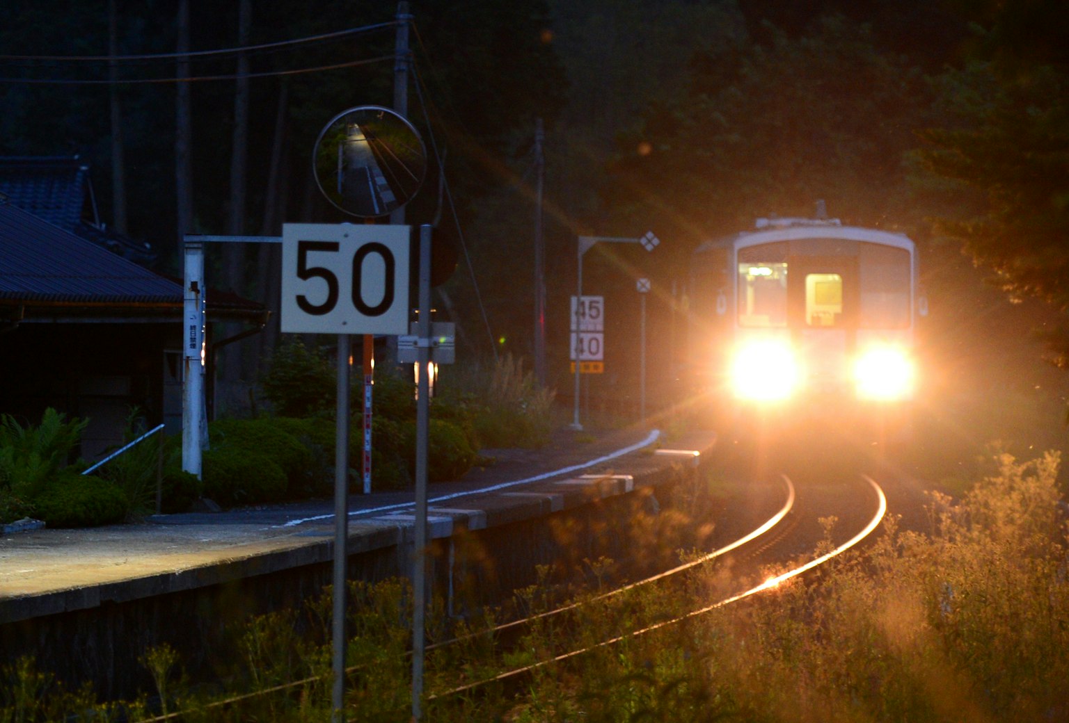 Train approaching a station at night with headlights and a speed limit sign reading 50