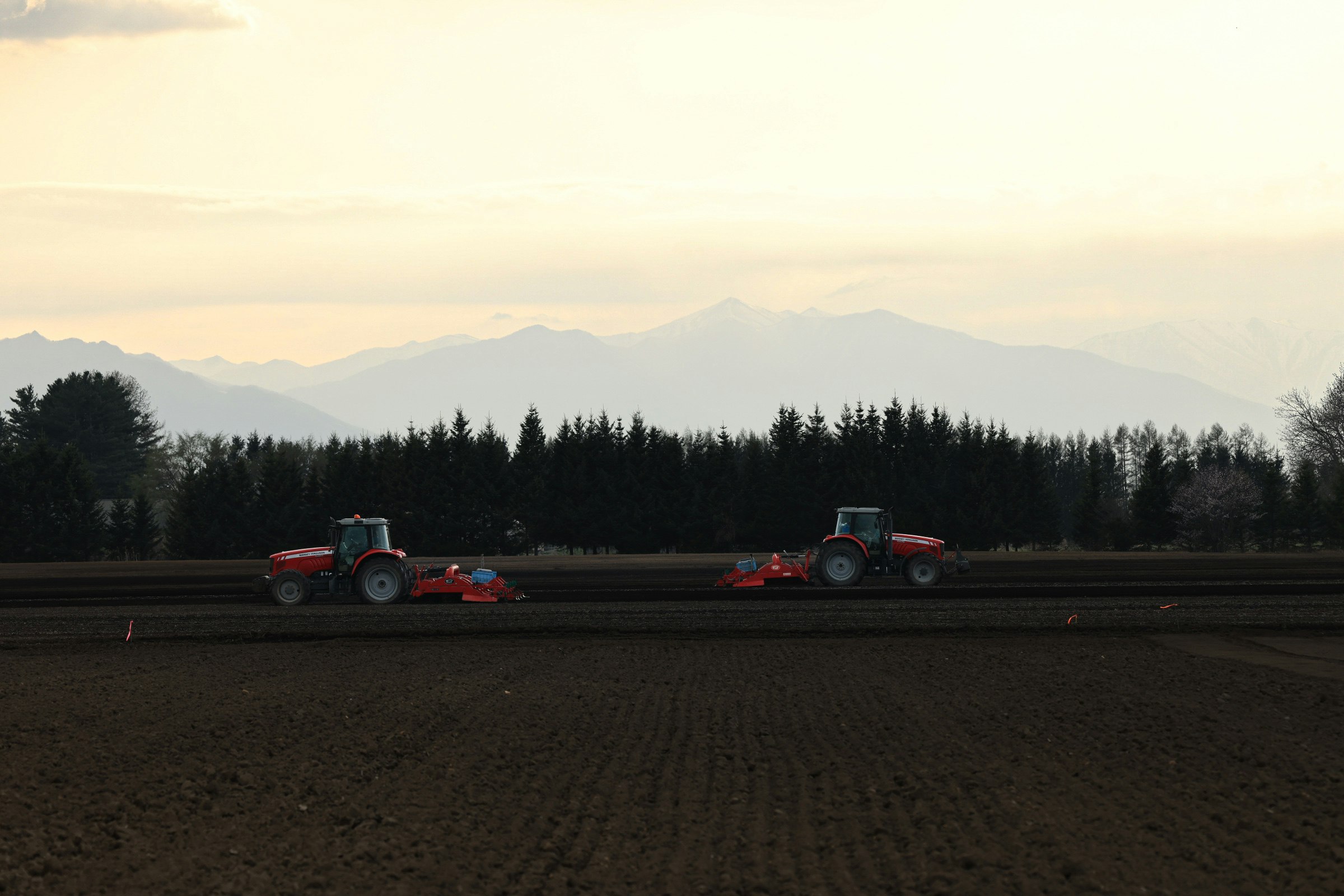 Red tractors driving across a field with distant mountains