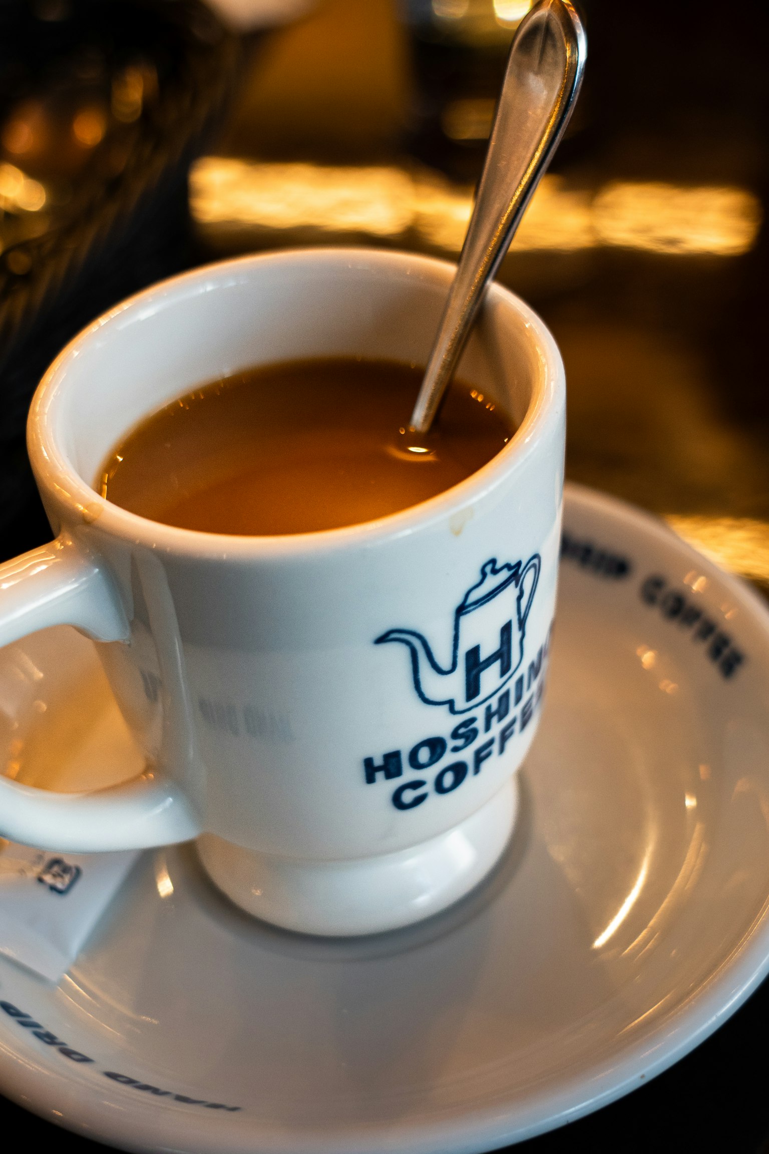 Secangkir kopi hangat dengan sendok di dalamnya di atas piring