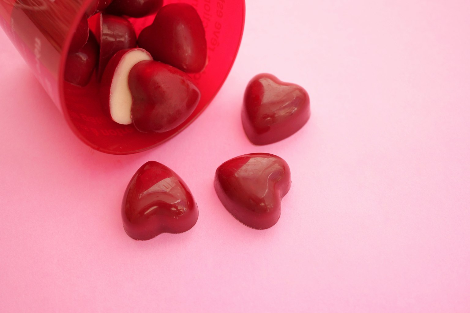 Rote herzförmige Bonbons auf einem rosa Hintergrund verteilt