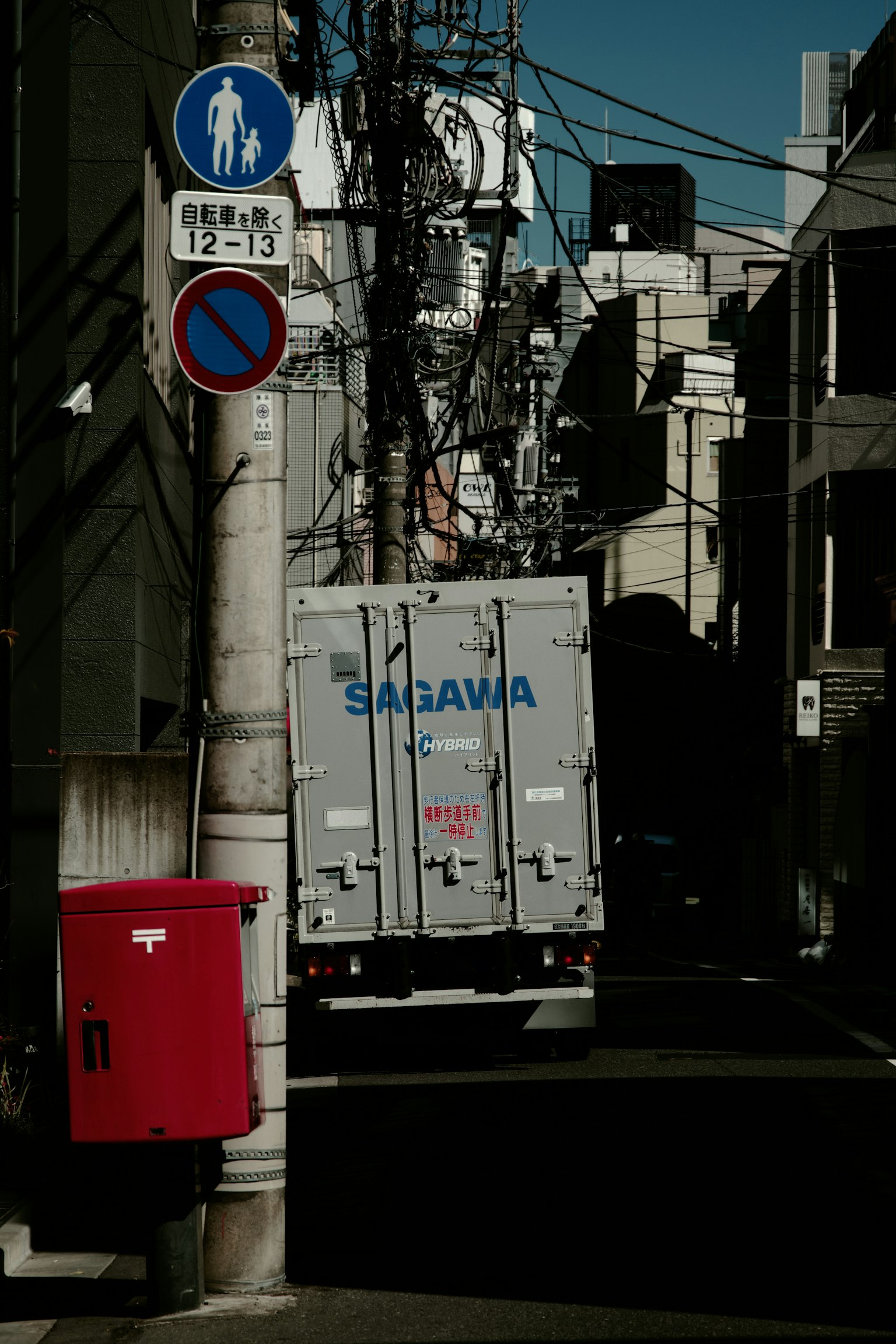 Vue d'un camion Saragawa garé dans une ruelle étroite avec une boîte aux lettres rouge