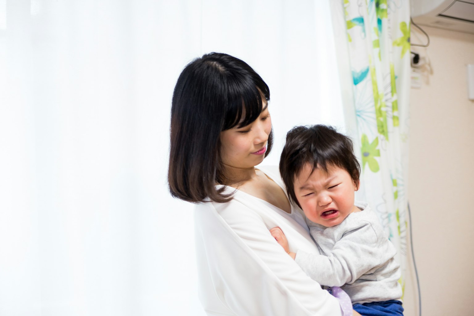 Người phụ nữ bế đứa trẻ khóc gần cửa sổ sáng
