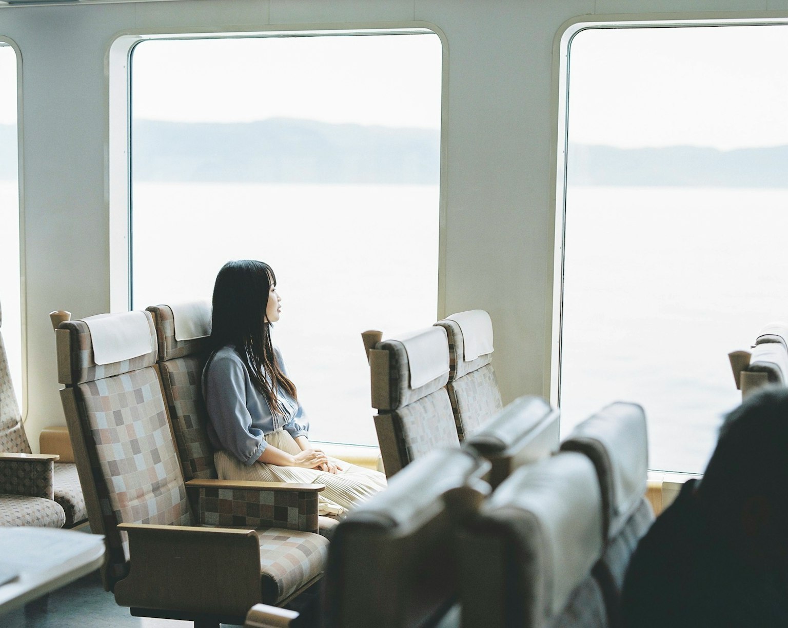 A woman sitting by the window on a ferry gazing at the sea