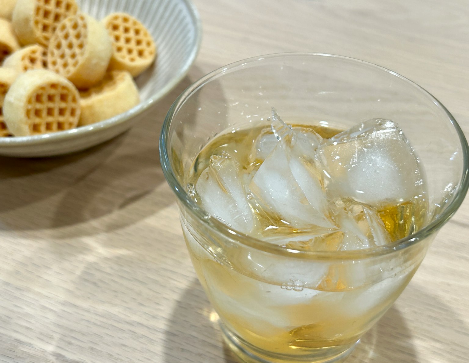 Un verre avec de la glace et une boisson à côté d'une assiette de petites gaufres