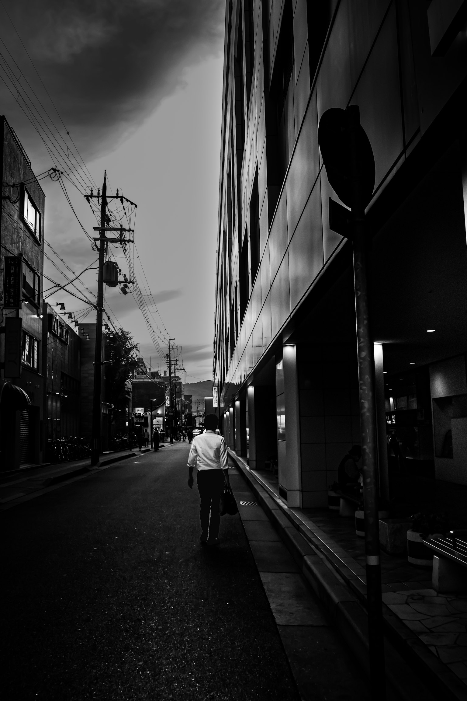A person walking down a black and white street with buildings and power lines