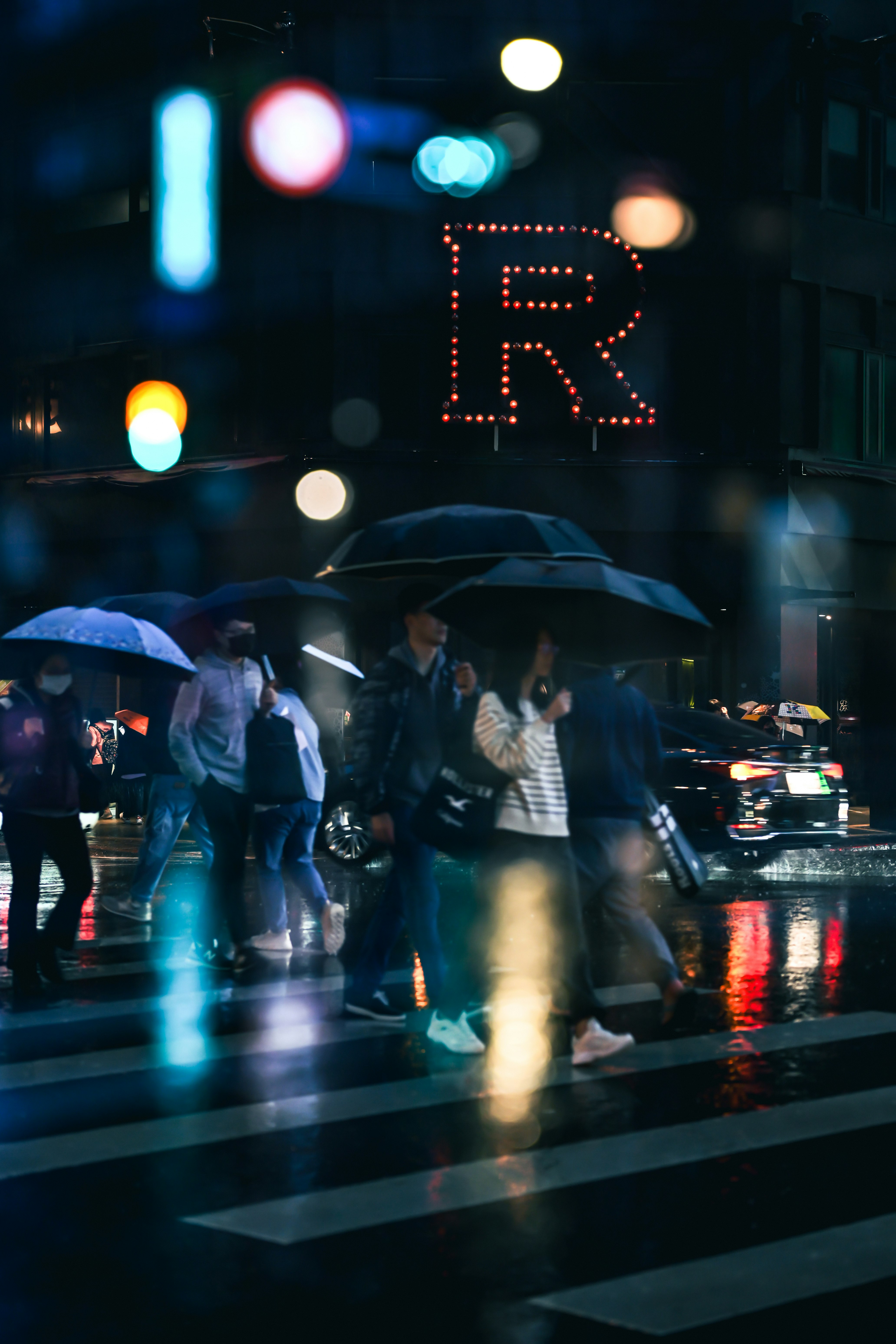 雨の夜のにぎやかな交差点で傘をさす人々の流れ