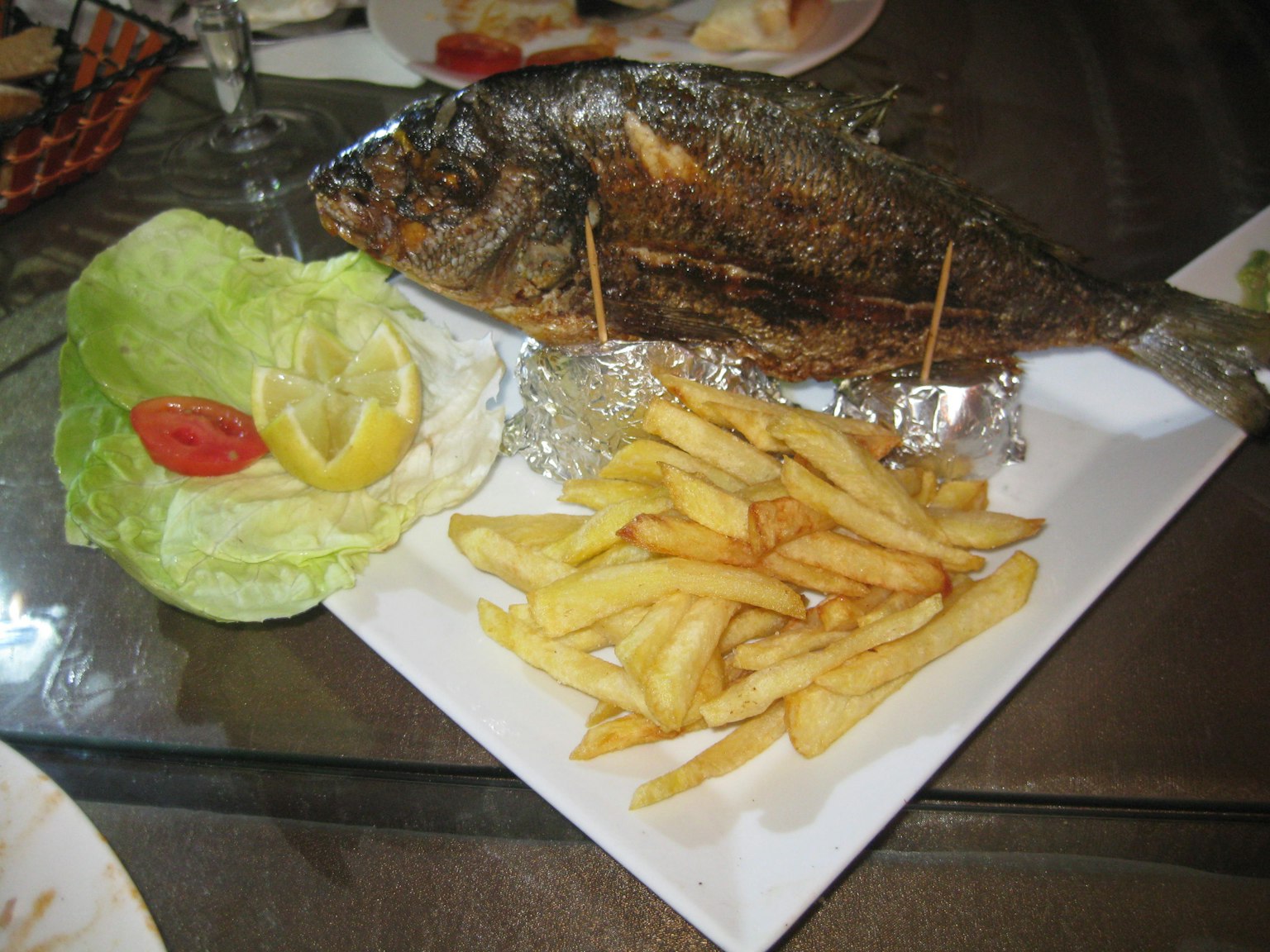 Grilled fish served with French fries garnished with fresh lettuce and tomatoes