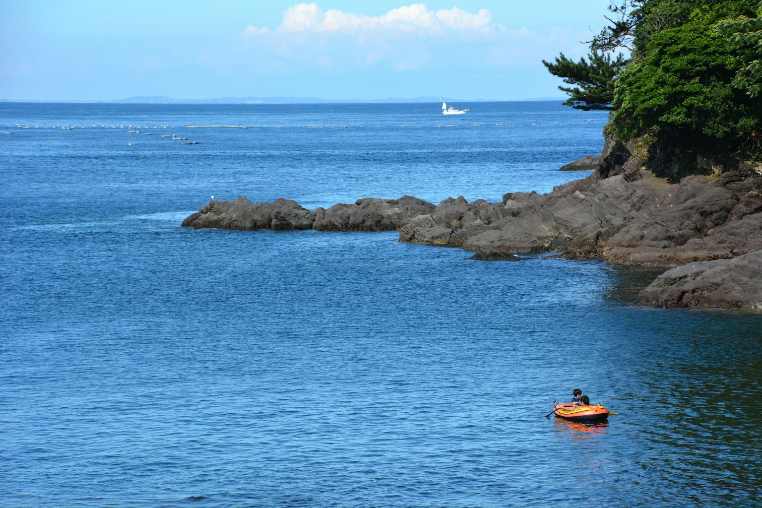 Kayak naranja en agua azul cerca de una costa rocosa con un velero a lo lejos