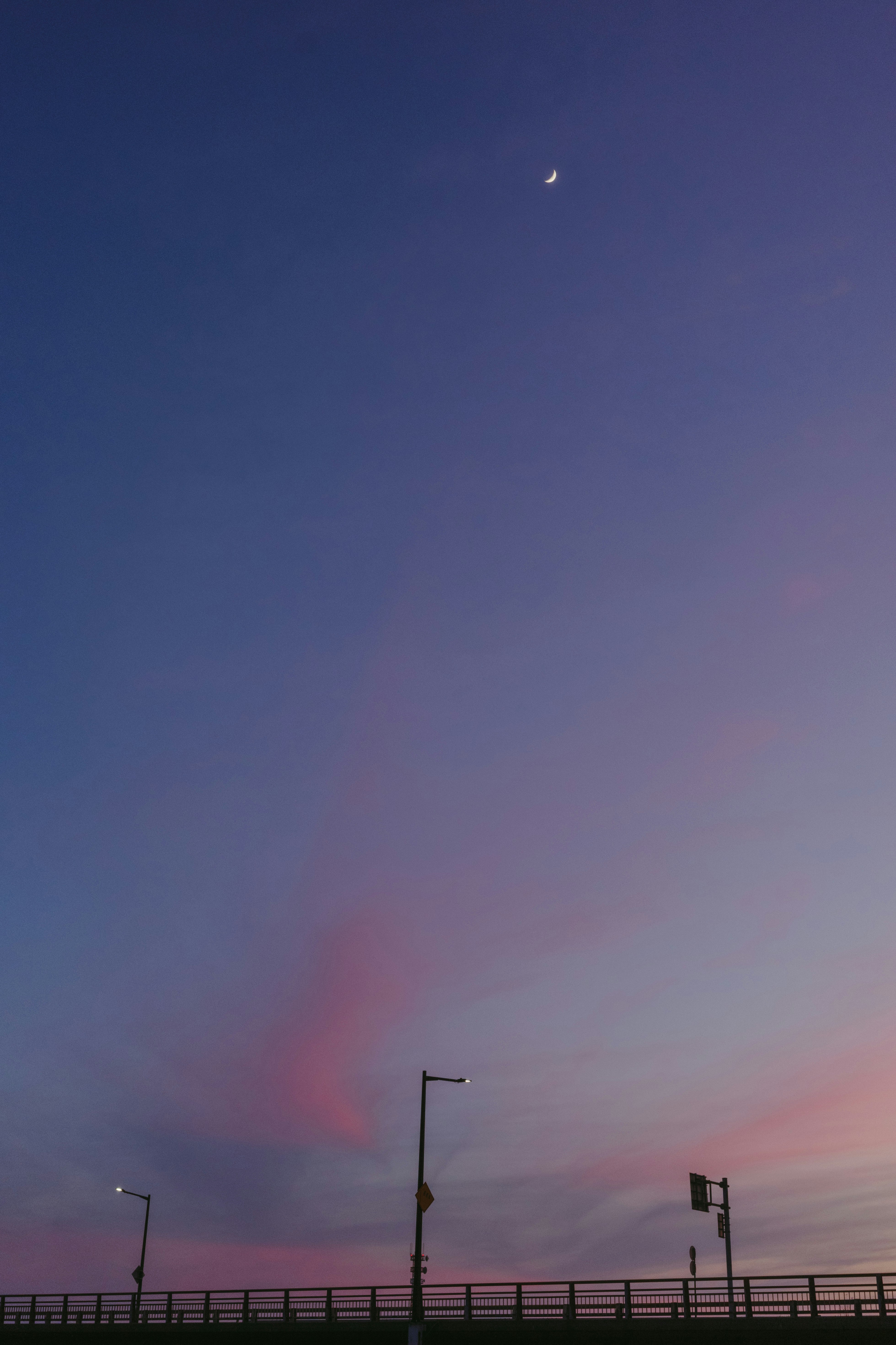 夕暮れの空と海辺の柵、月が浮かぶブルーアワーの景色