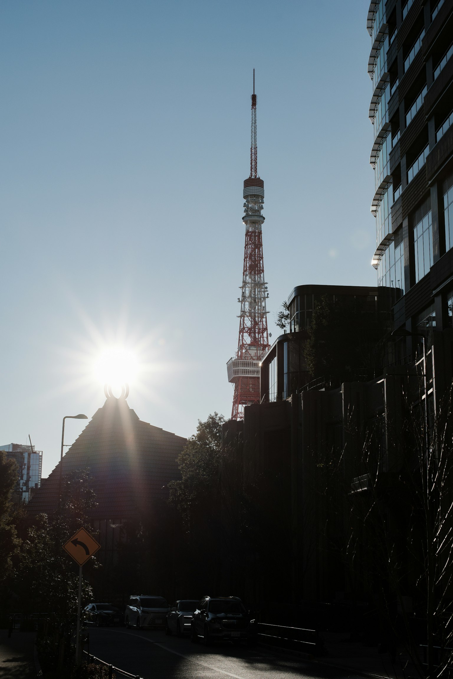 Silhouette of Tokyo Tower against the sun with surrounding buildings and street