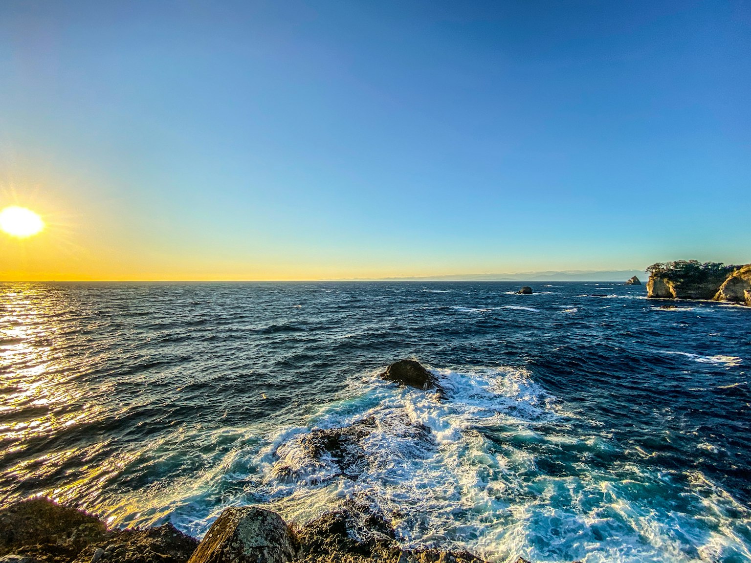 Atardecer sobre el océano con olas rompiendo contra la costa rocosa