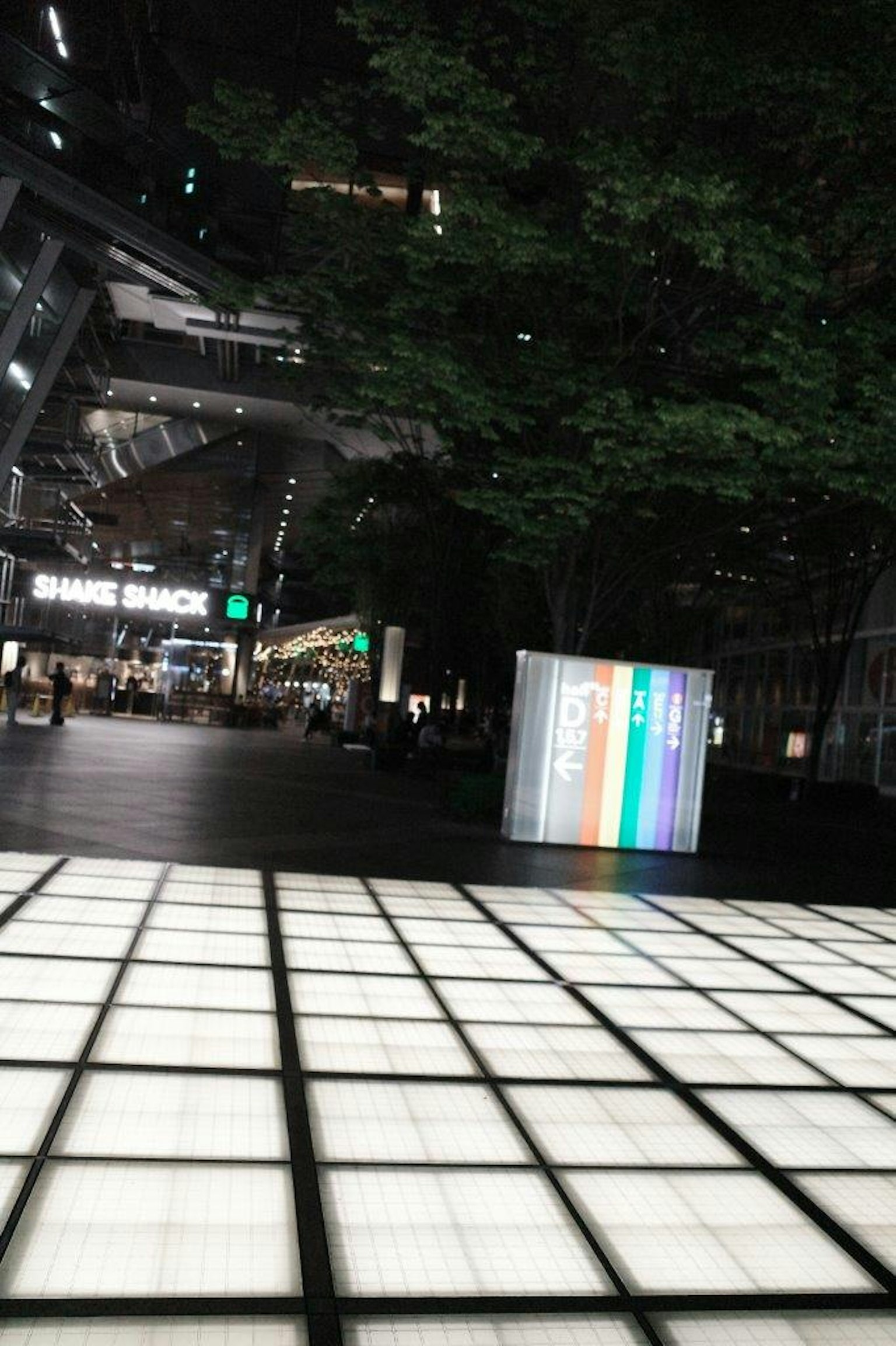 Illuminated tiles in a city square at night with a colorful display box