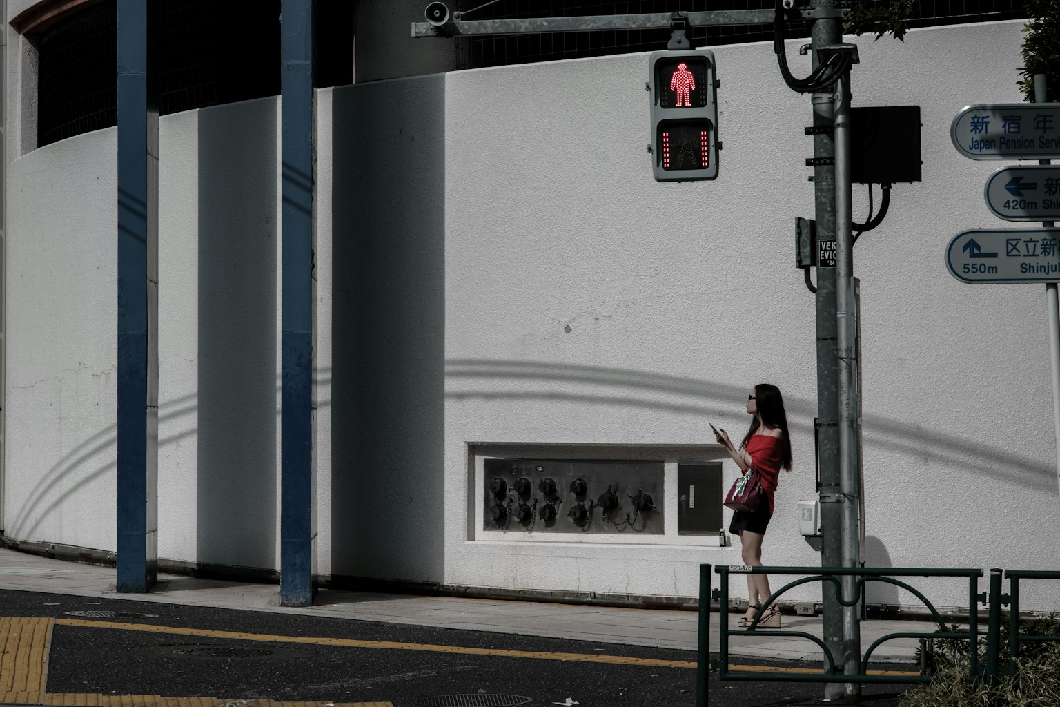 A woman standing at a red traffic light by a white wall