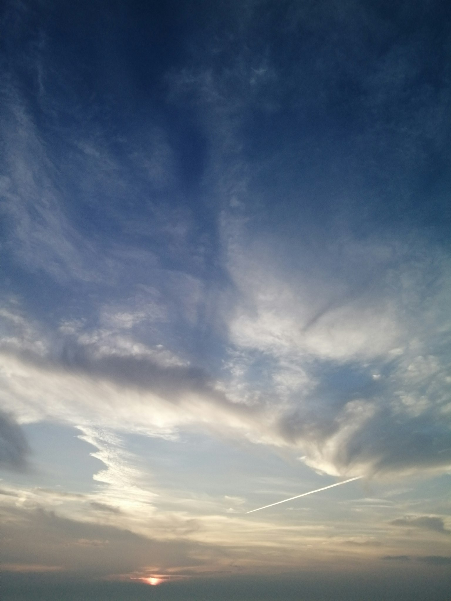 Vast blue sky with wispy clouds and a glowing sunset