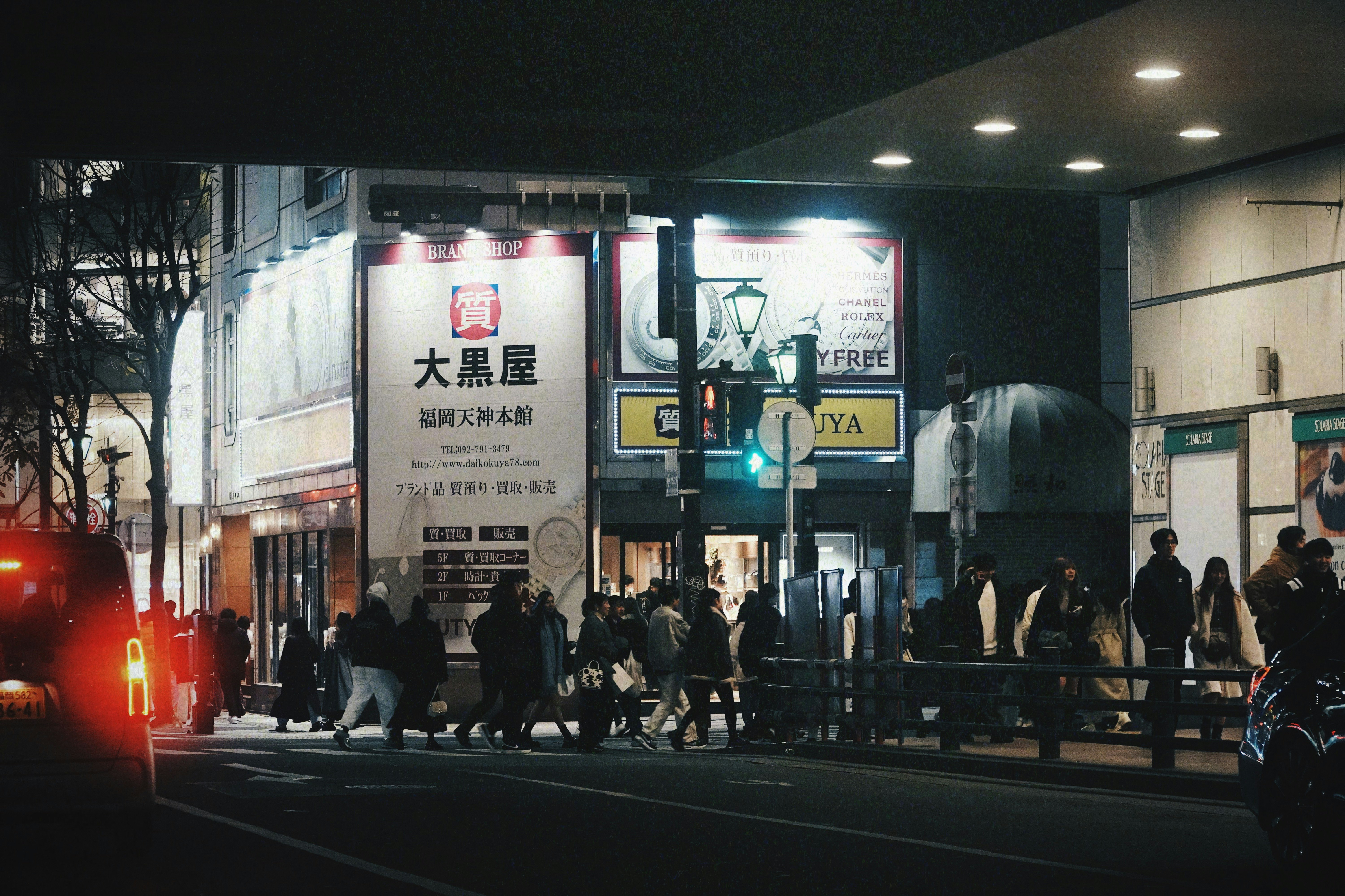 夜の街角で人が行き交うバス停前の看板と街灯の光