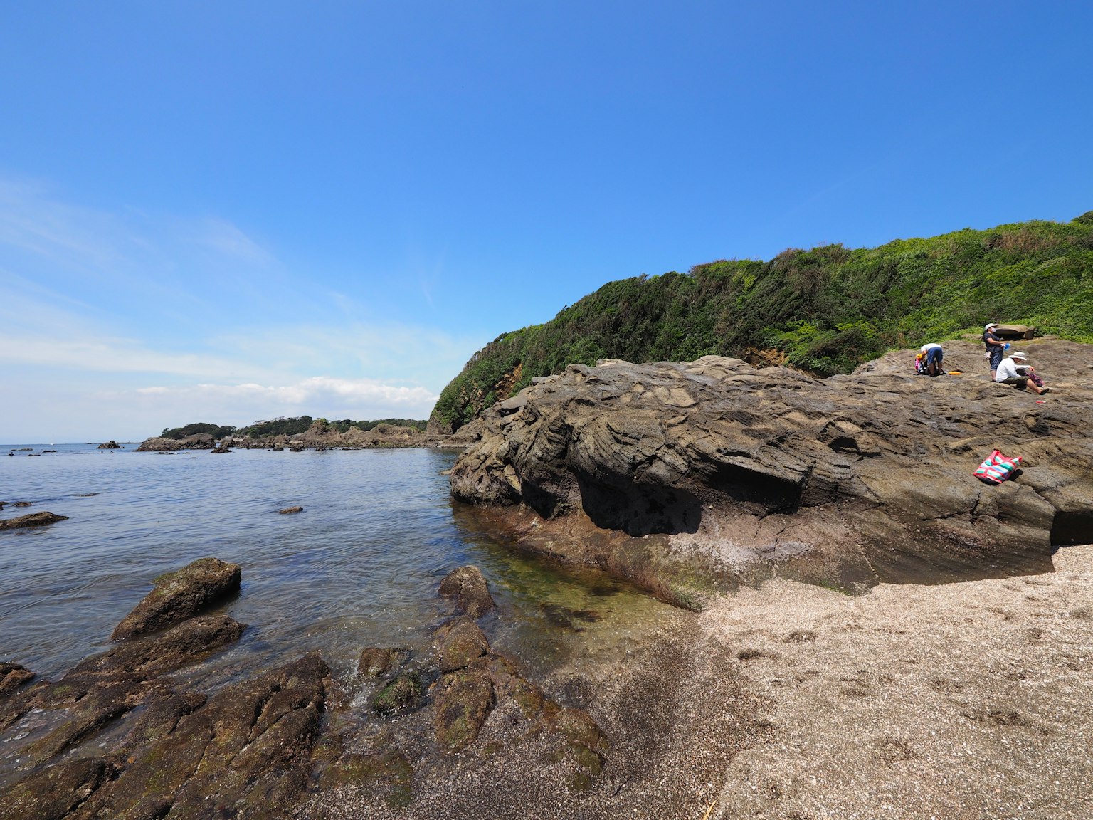 陽光明媚的海灘場景，岩石海岸和綠色山丘