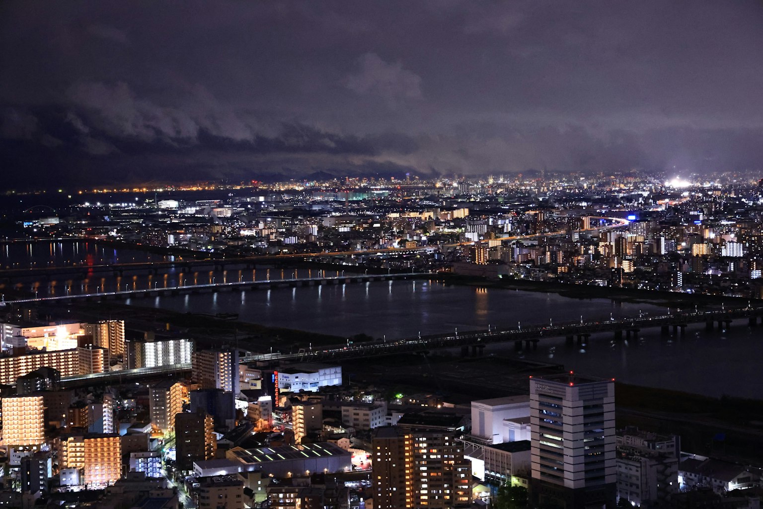 Paysage urbain nocturne avec une rivière et un pont illuminé par les lumières de la ville