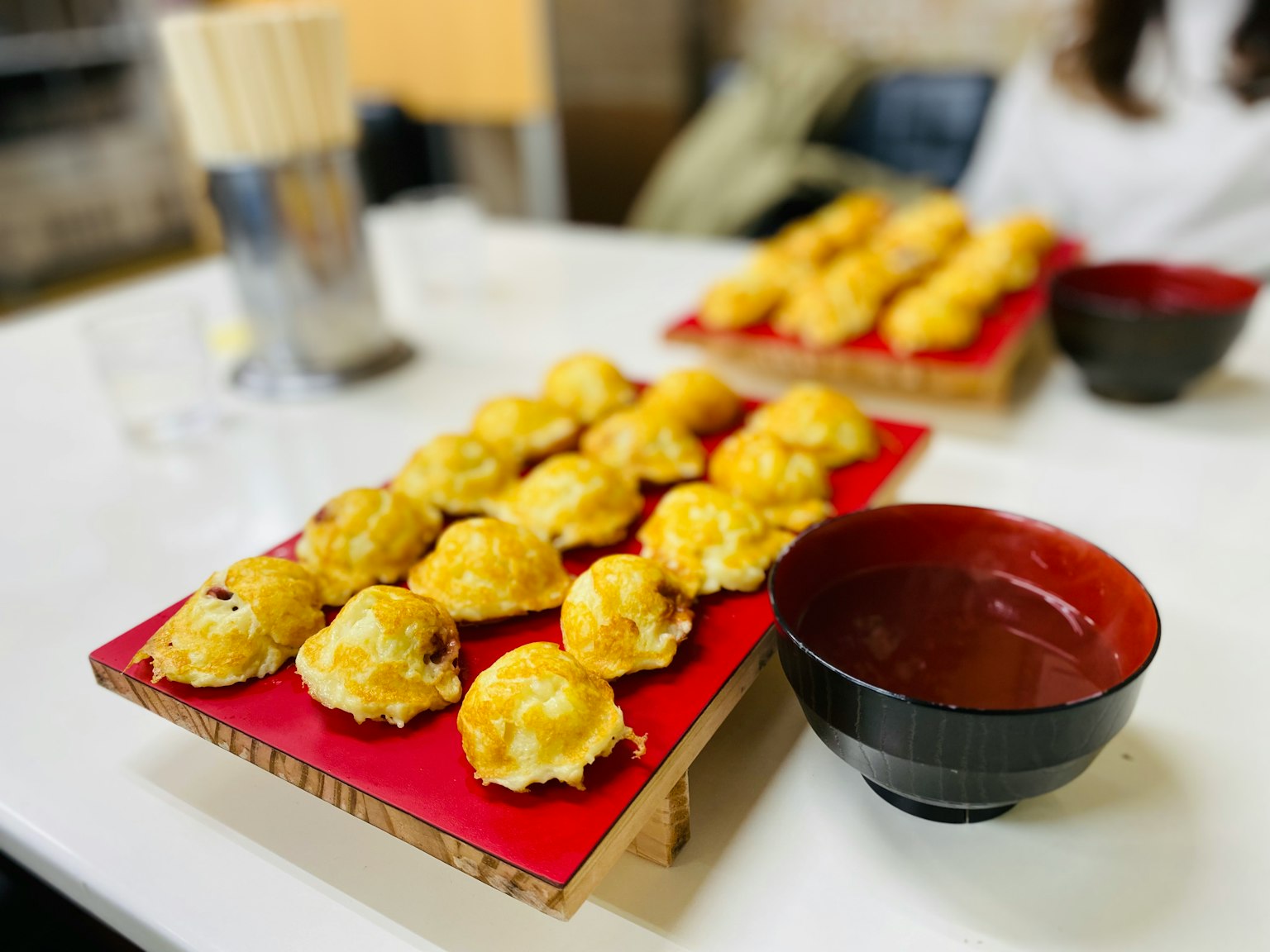 Takoyaki auf einem roten Teller mit einer schwarzen Schüssel angeordnet