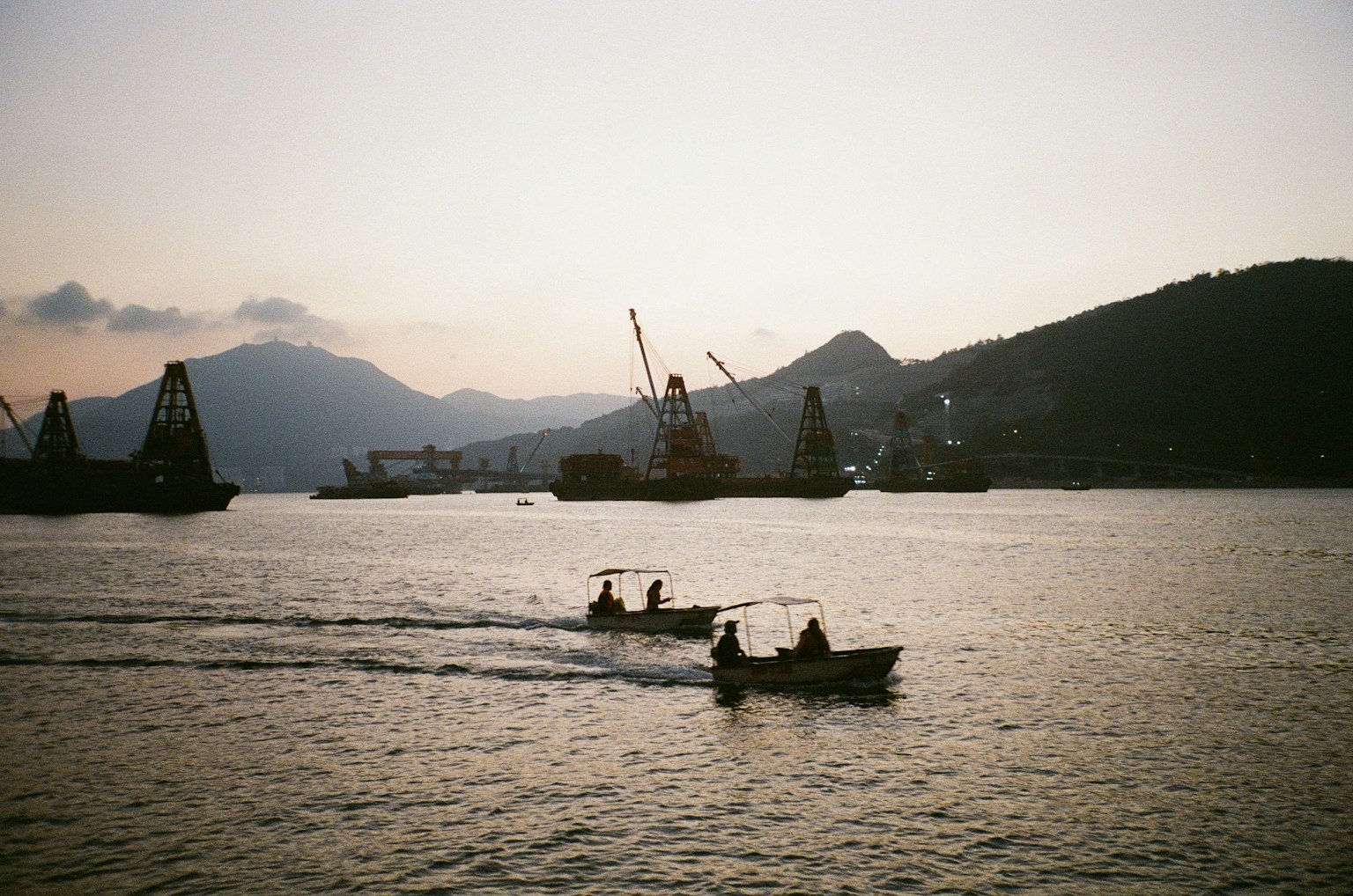夕暮れの海で小舟が漕ぎ進む風景 山々とクレーンが背景に見える