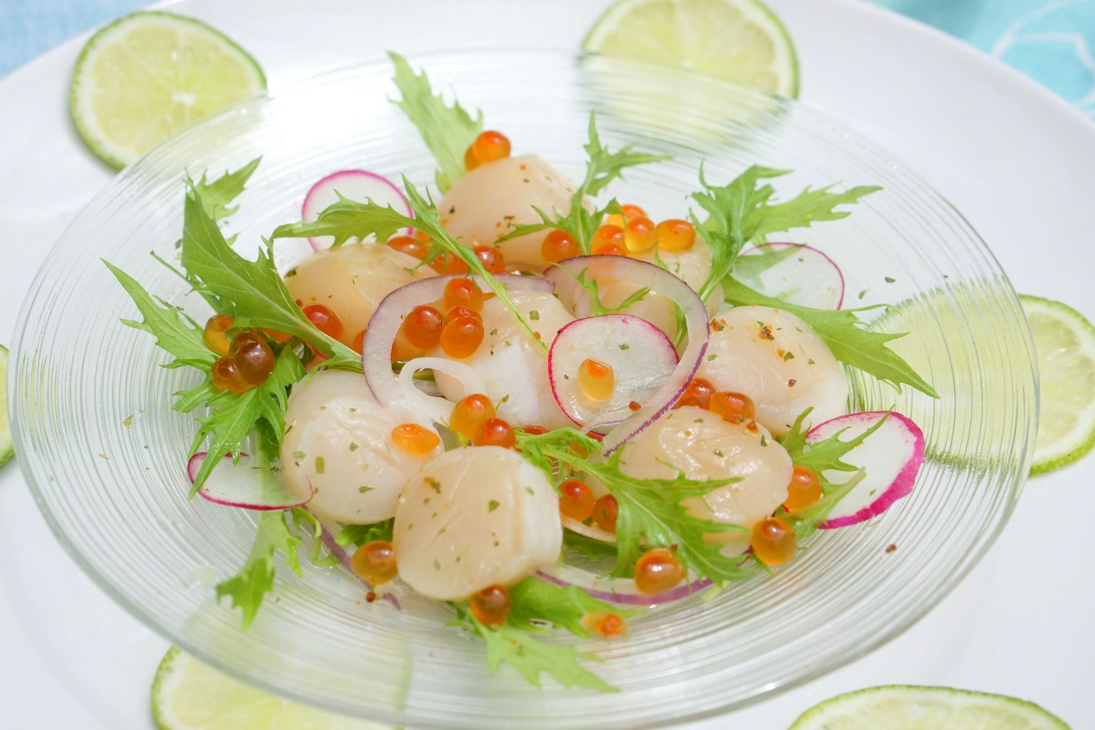 Frischer Jakobsmuscheln- und Lachsrogen-Salat schön präsentiert mit Limettenscheiben und Kräutern