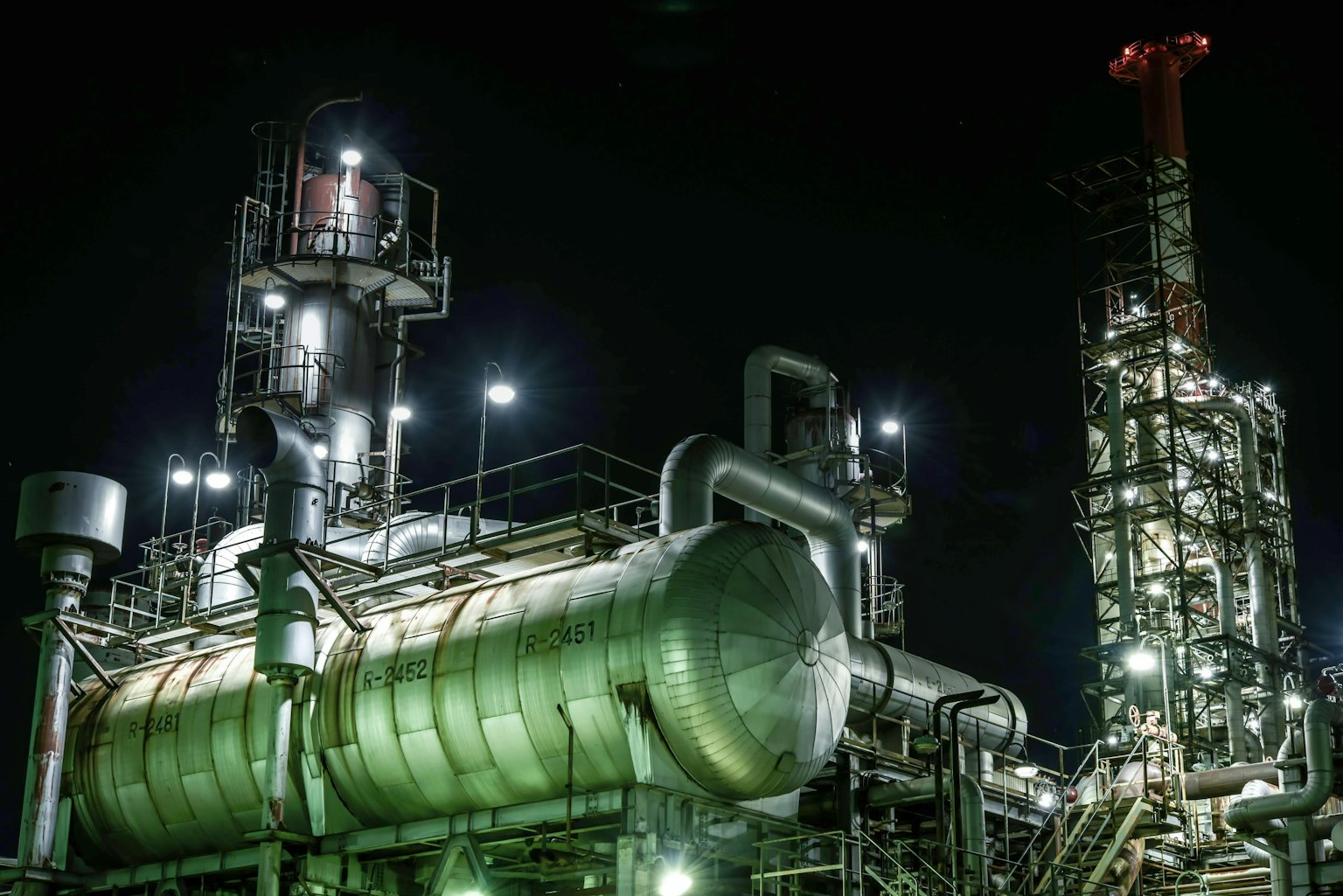 Scène industrielle nocturne avec des tuyaux et des réservoirs éclairés
