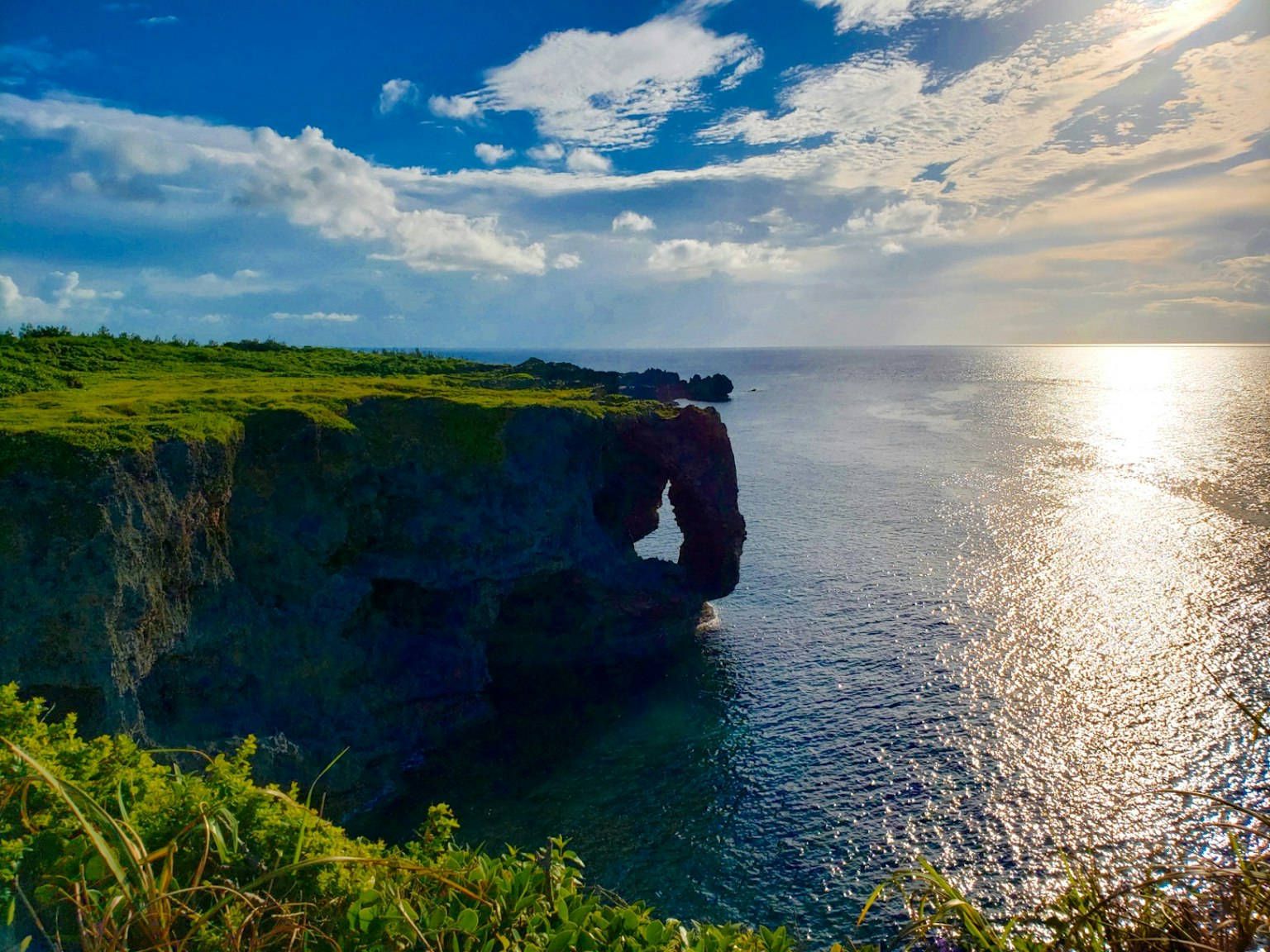 Lengkungan alami di tebing hijau dikelilingi langit biru dan lautan